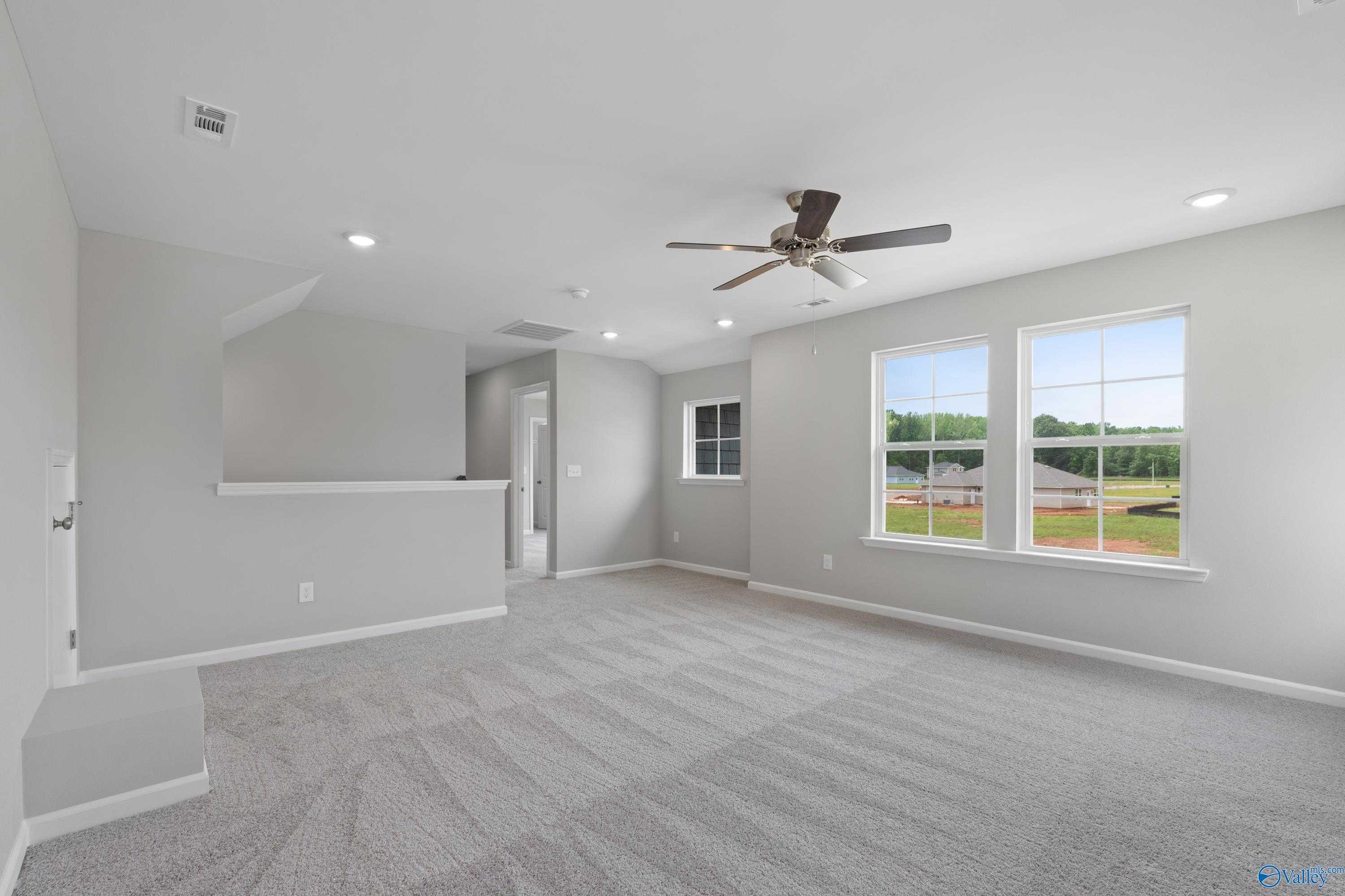 Spacious upstairs loft with gray carpet, ceiling fan, and large windows overlooking green fields in Davidson Homes The Stella, Hazel Green, Alabama
