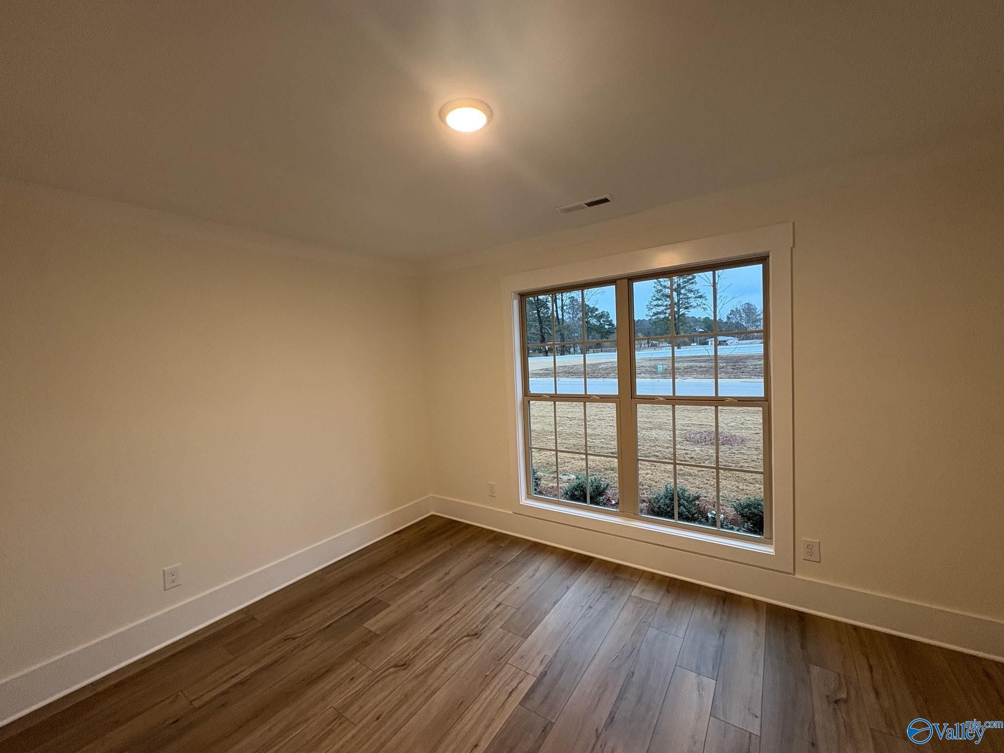 Bright bedroom with neutral walls, hardwood floors, and large window to wooded view in Davidson Homes The Daphne C, Arab, Alabama