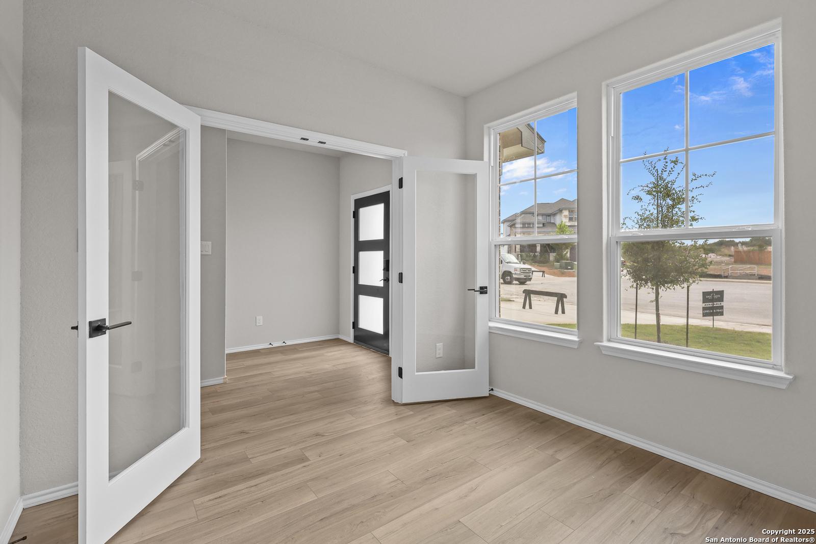 Bright flex room with open glass French doors, light wood floors, and large windows to suburban front yard in Davidson Homes The Murray J, San Antonio