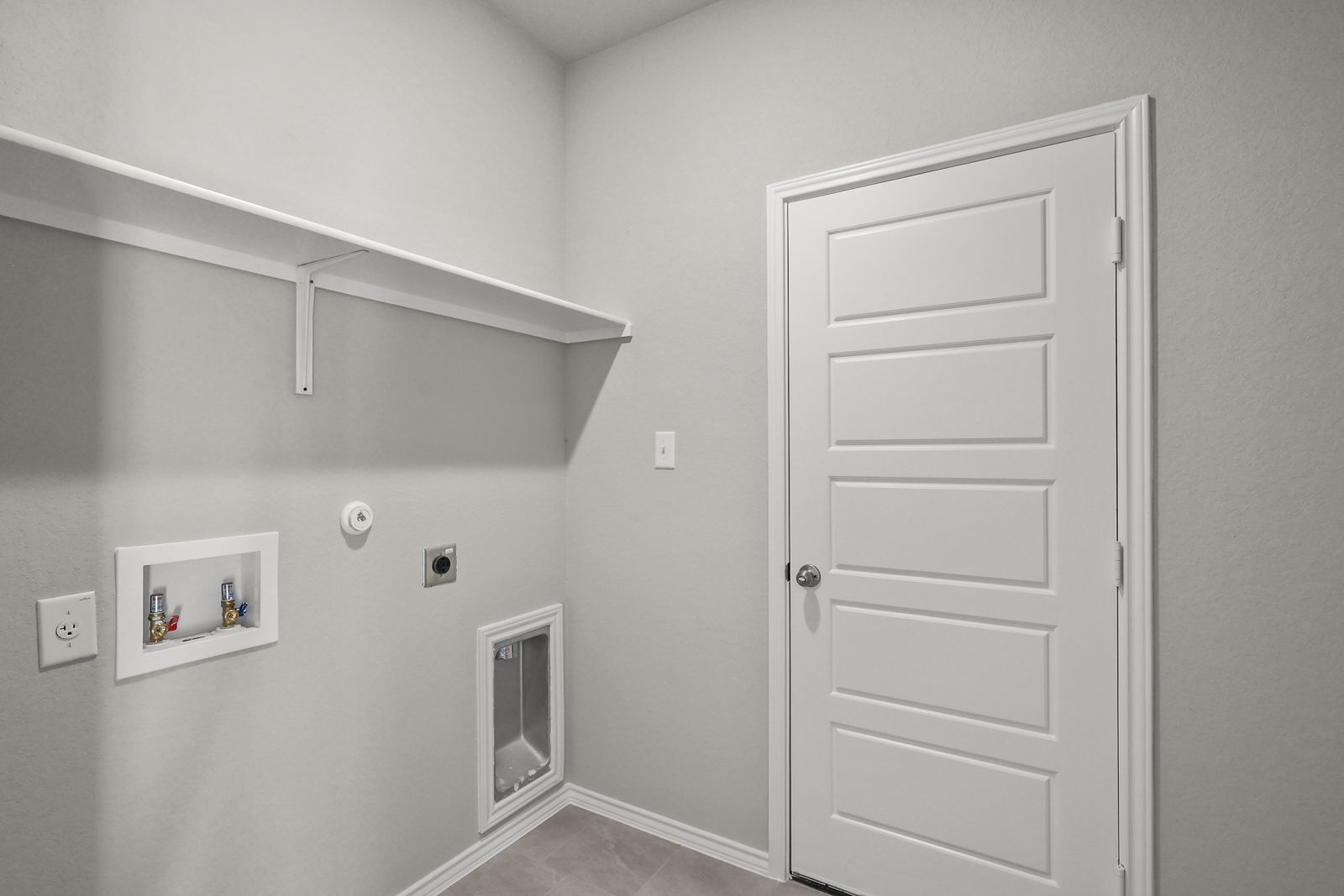 Laundry room in The Arroyo home design featuring washer and dryer connections, shelving, and neutral interior finishes.