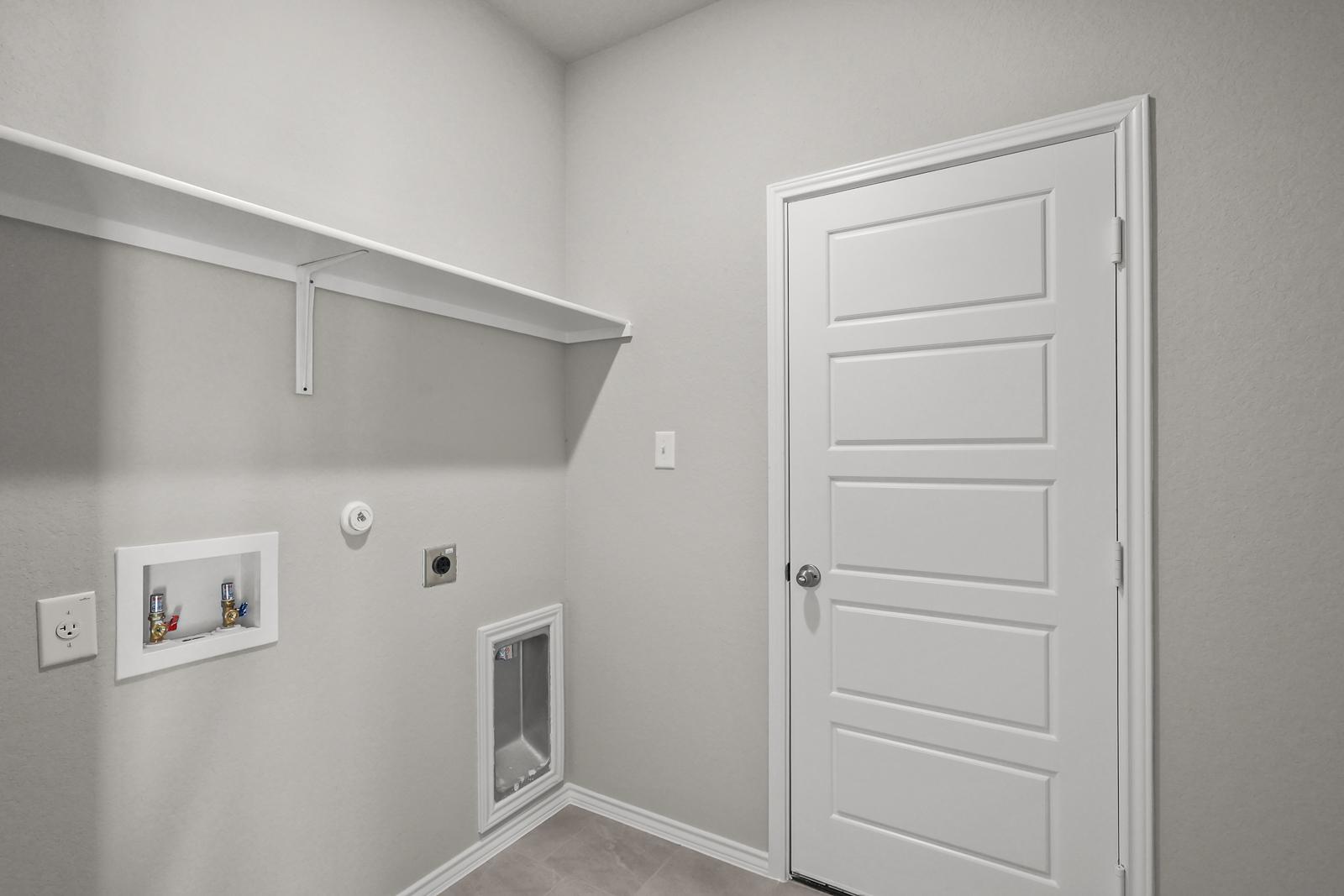 Laundry room in The Arroyo home design featuring washer and dryer connections, shelving, and neutral interior finishes.
