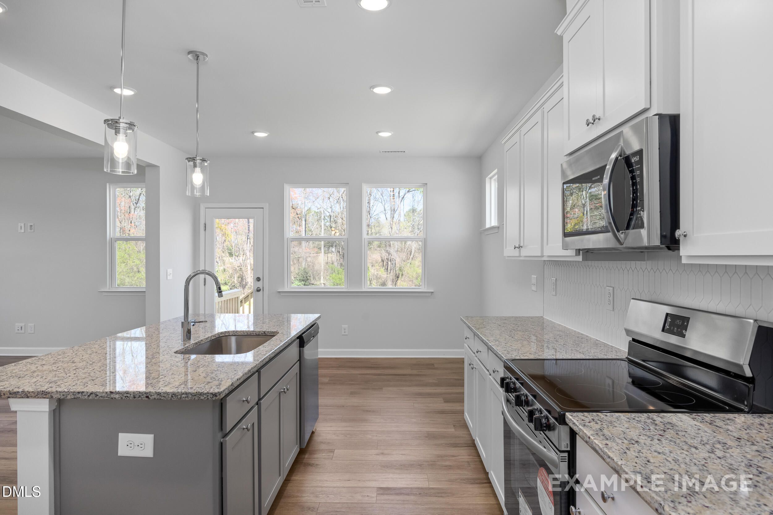 Modern kitchen with granite island, white cabinets, and stainless appliances in The Gavin A floor plan, Lillington, NC.