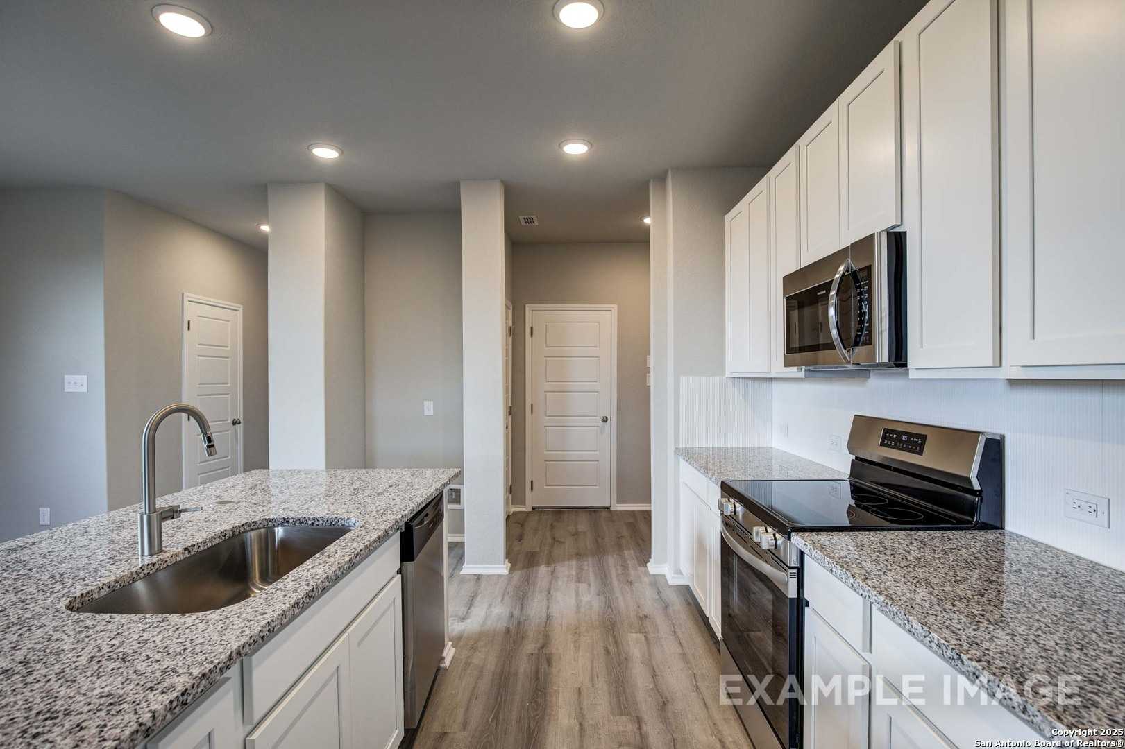 Modern open-concept kitchen with white cabinets, granite island sink, stainless appliances in Davidson Homes The Blanco C, San Antonio