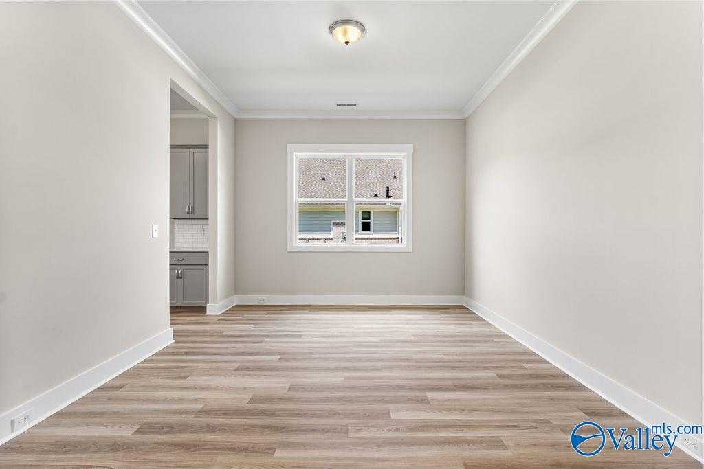 Spacious empty living room with luxury vinyl plank flooring, large window, and adjacent kitchen in Evermore Homes The Oxford, Owens Cross Roads, AL