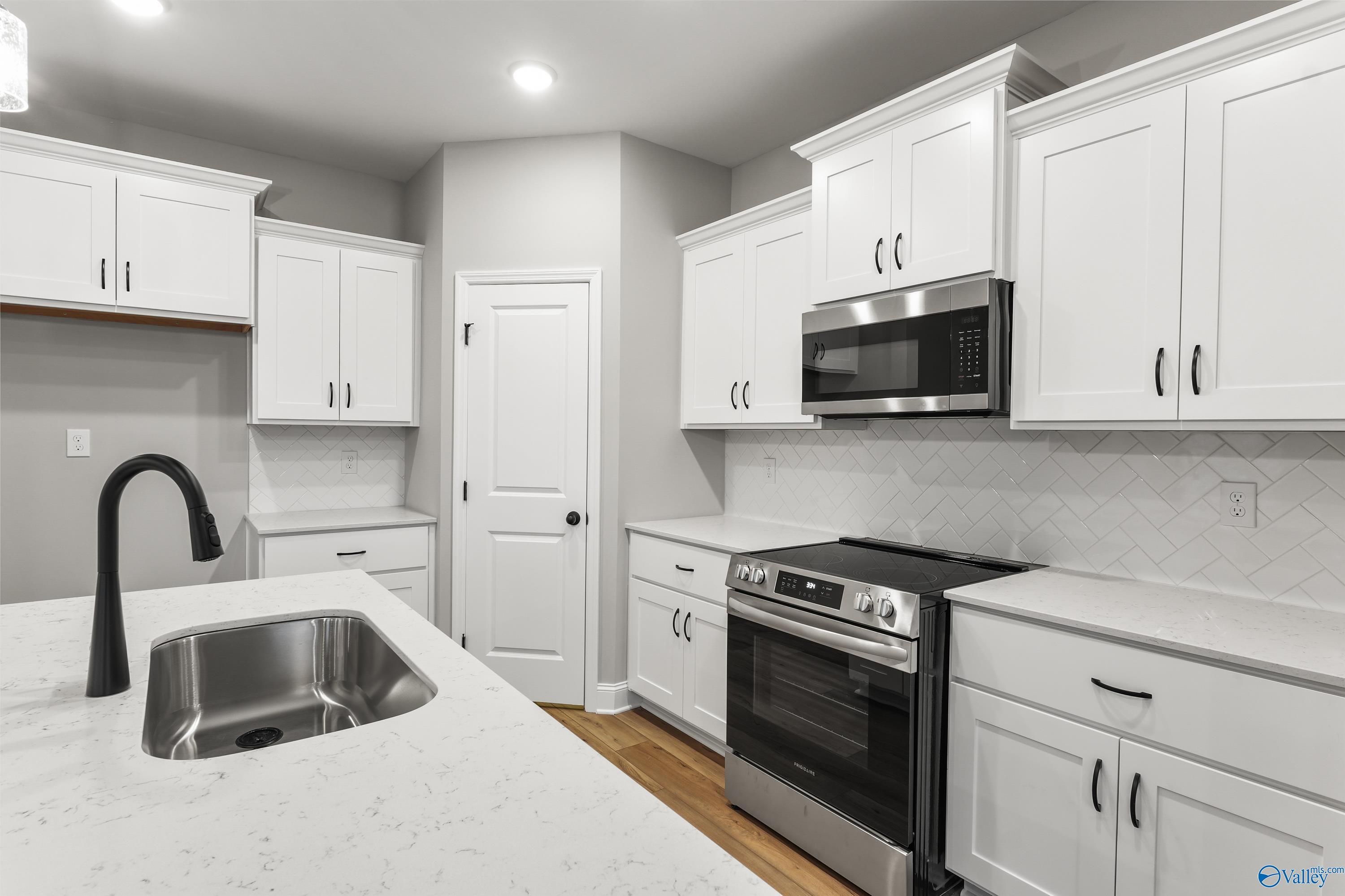 Modern white kitchen with quartz island, stainless appliances, and subway tile backsplash in The Asheville C, Meridianville, AL