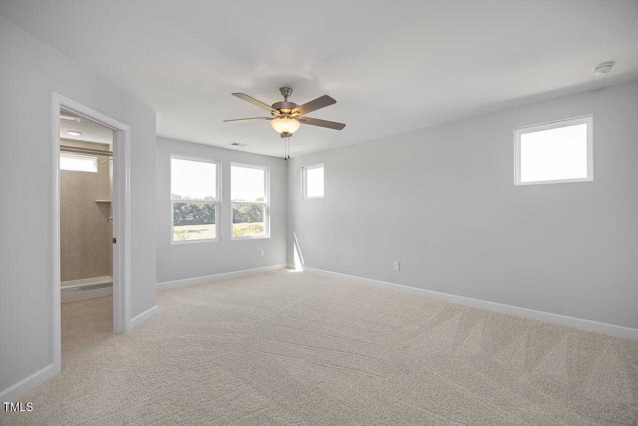 Spacious secondary bedroom with beige carpet, ceiling fan, large windows, and ensuite bath in Davidson Homes The Graham, Fuquay-Varina, NC