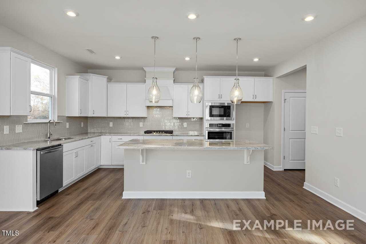 Modern open-concept kitchen with white cabinets, granite island, stainless appliances in The Hickory II B by Davidson Homes, Lillington, NC