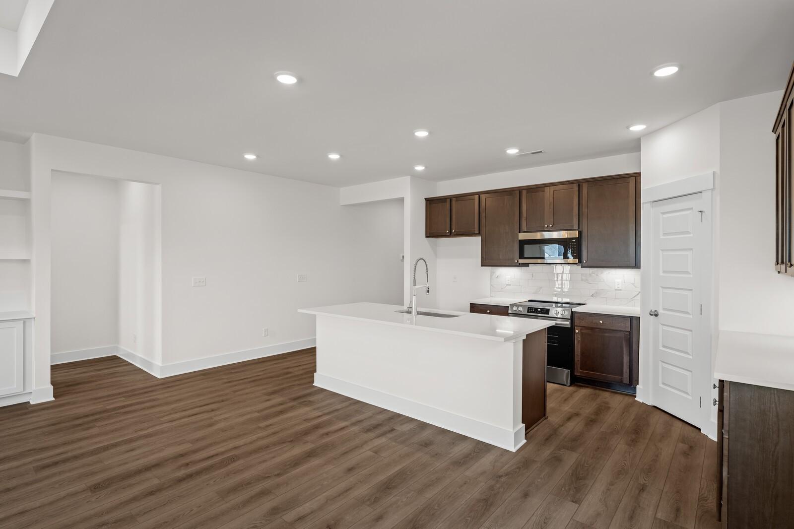 Modern kitchen with white island, dark cabinetry, and wood-style flooring in The Cottonwood floor plan, Woods Crossing.