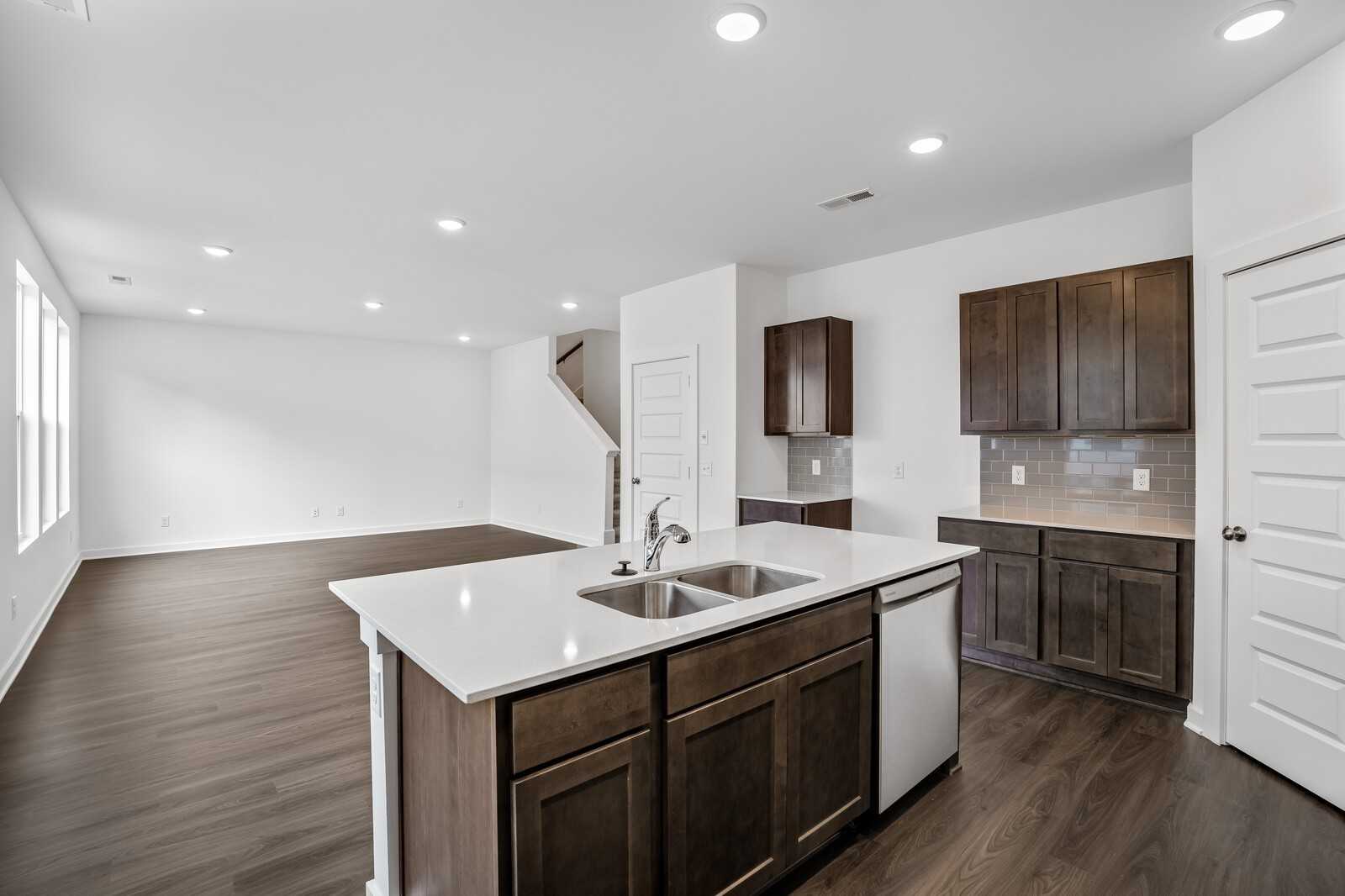 Modern open-concept kitchen with white quartz island, farmhouse sink, shaker cabinets, and hardwood floors in The Logan C, White House, TN