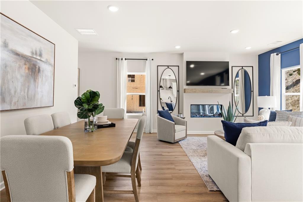 Open-concept living and dining room with wooden table, white sofa, gas fireplace, and blue accents in Davidson Homes The Burton C, Canton, Georgia