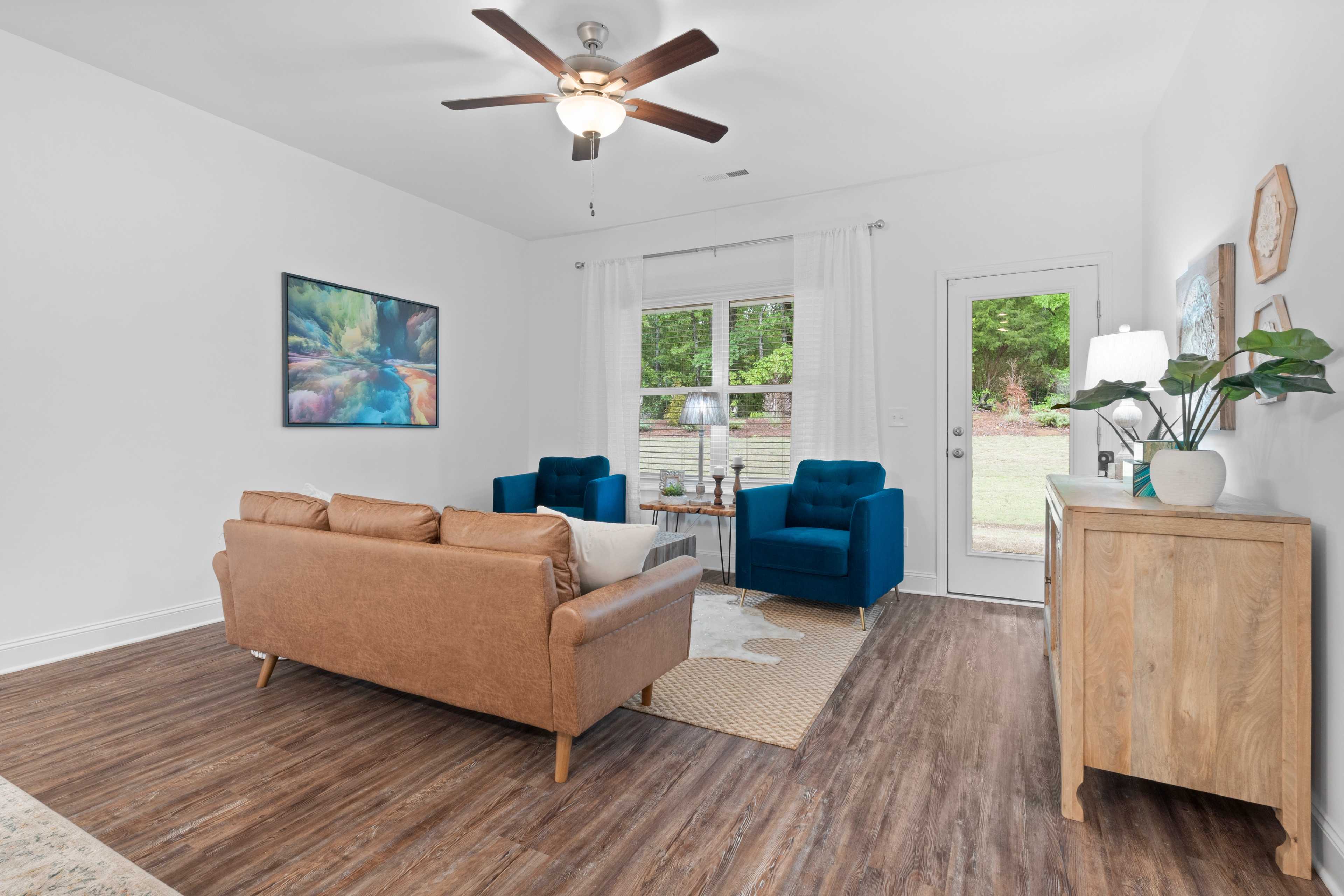 Spacious living room at The Retreat at Hollon Meadow in Decatur Alabama with brown leather sofa blue armchairs hardwood floors and French doors