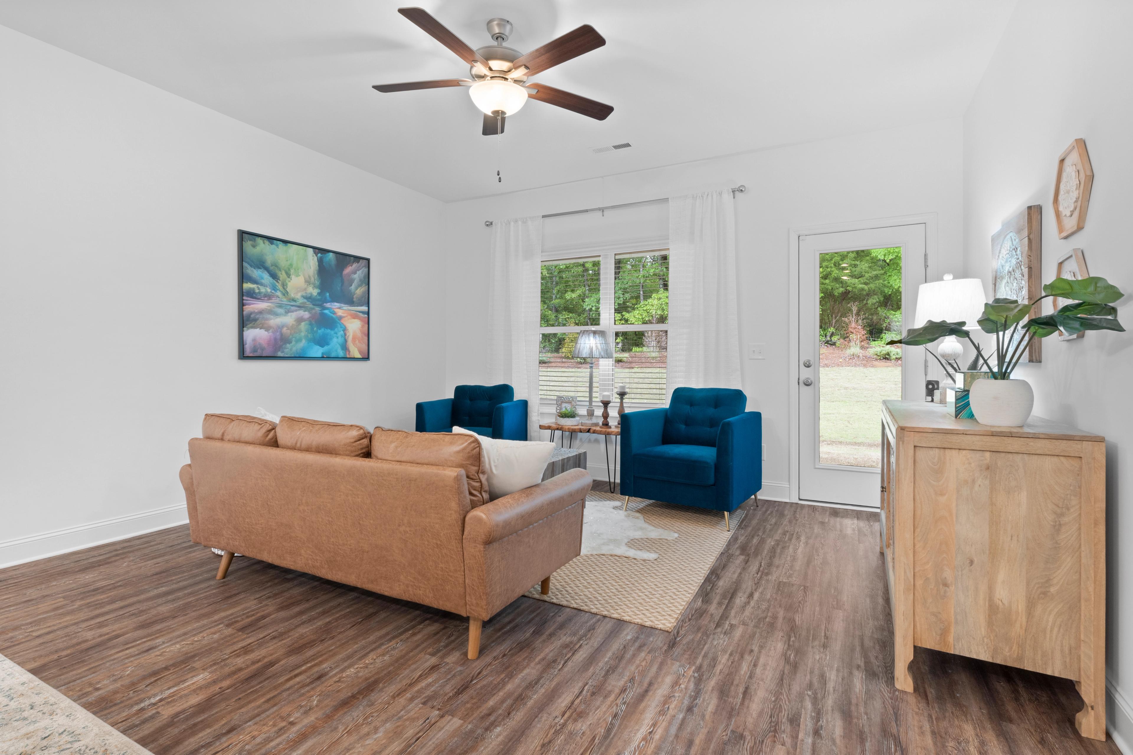 Spacious living room in The Cumberland home design with tan leather sofa, blue velvet chairs, ceiling fan, and hardwood floors