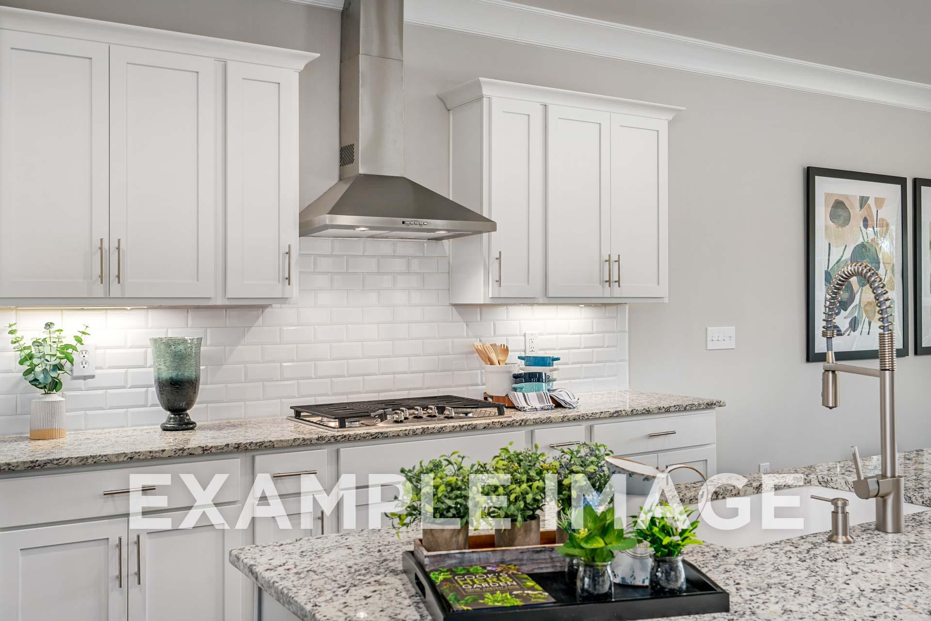 Modern white kitchen in The Harrison B with granite island, subway tile backsplash, stainless steel hood, and potted plants