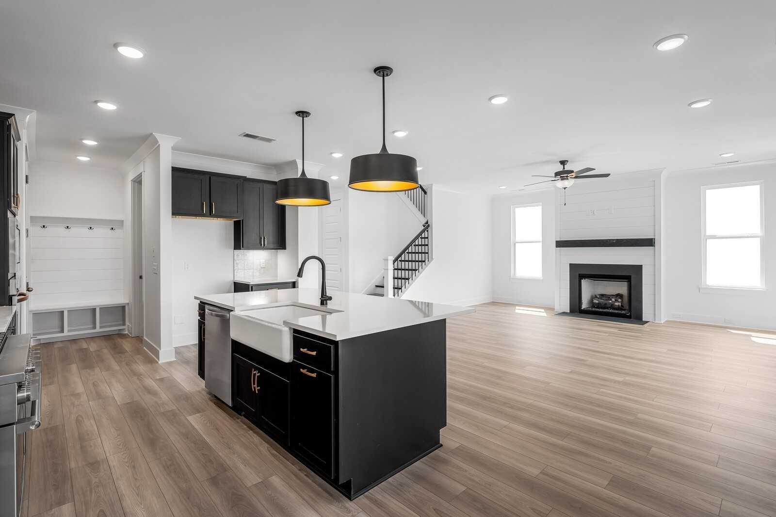 Open-concept kitchen with black cabinets, white quartz island, farmhouse sink, and adjacent family room featuring gas fireplace in The Hathaway floor plan, Murfreesboro, TN