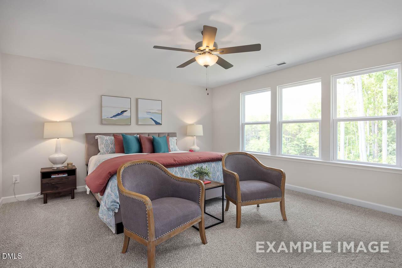 Cozy master bedroom with king bed, armchairs, ceiling fan, and large windows in Davidson Homes The Willow D, Lillington, NC