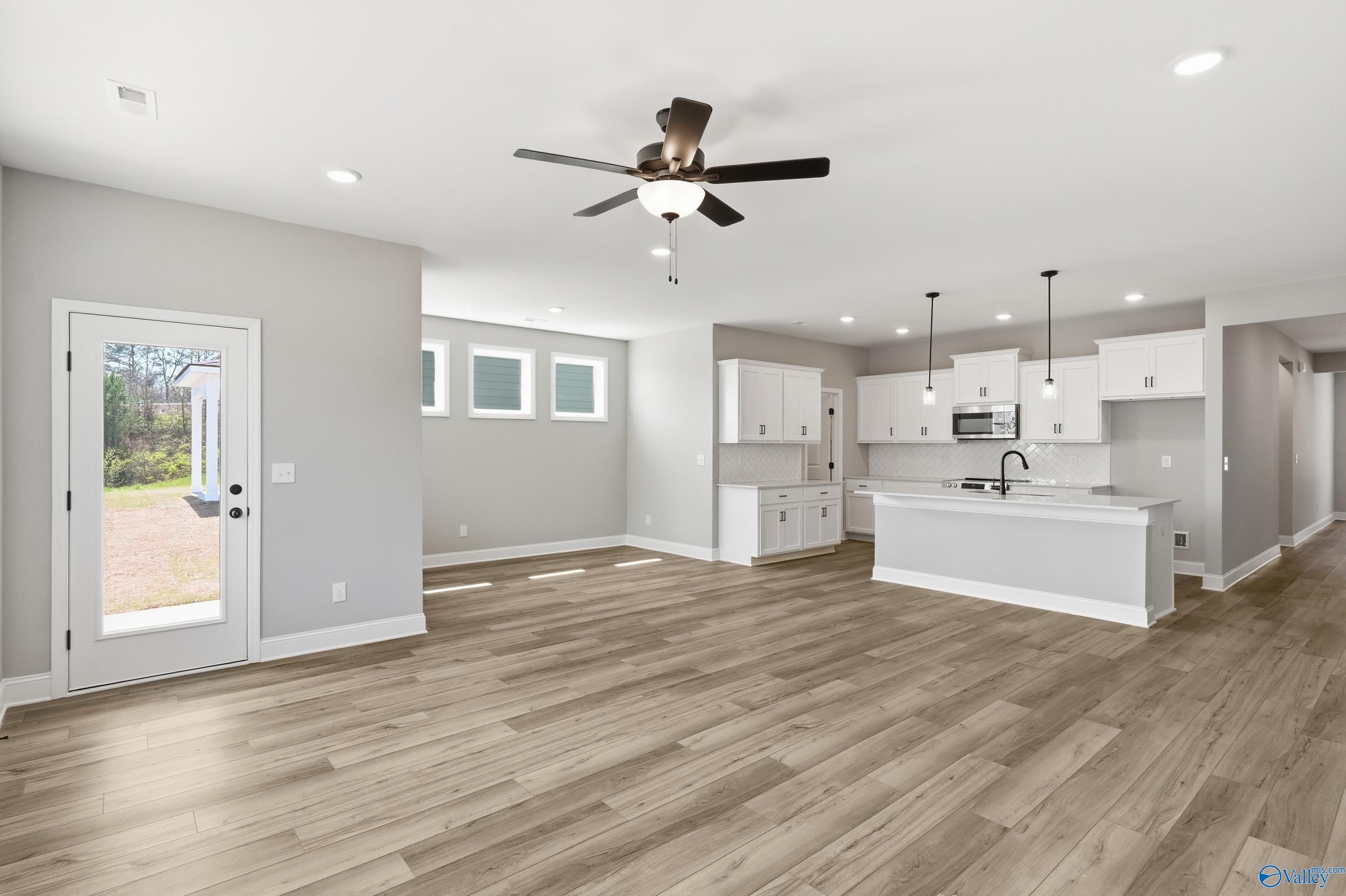Open-concept kitchen-living area with white cabinets, stainless appliances, wood floors, and ceiling fan in The Laurel K by Davidson Homes, Cullman, AL