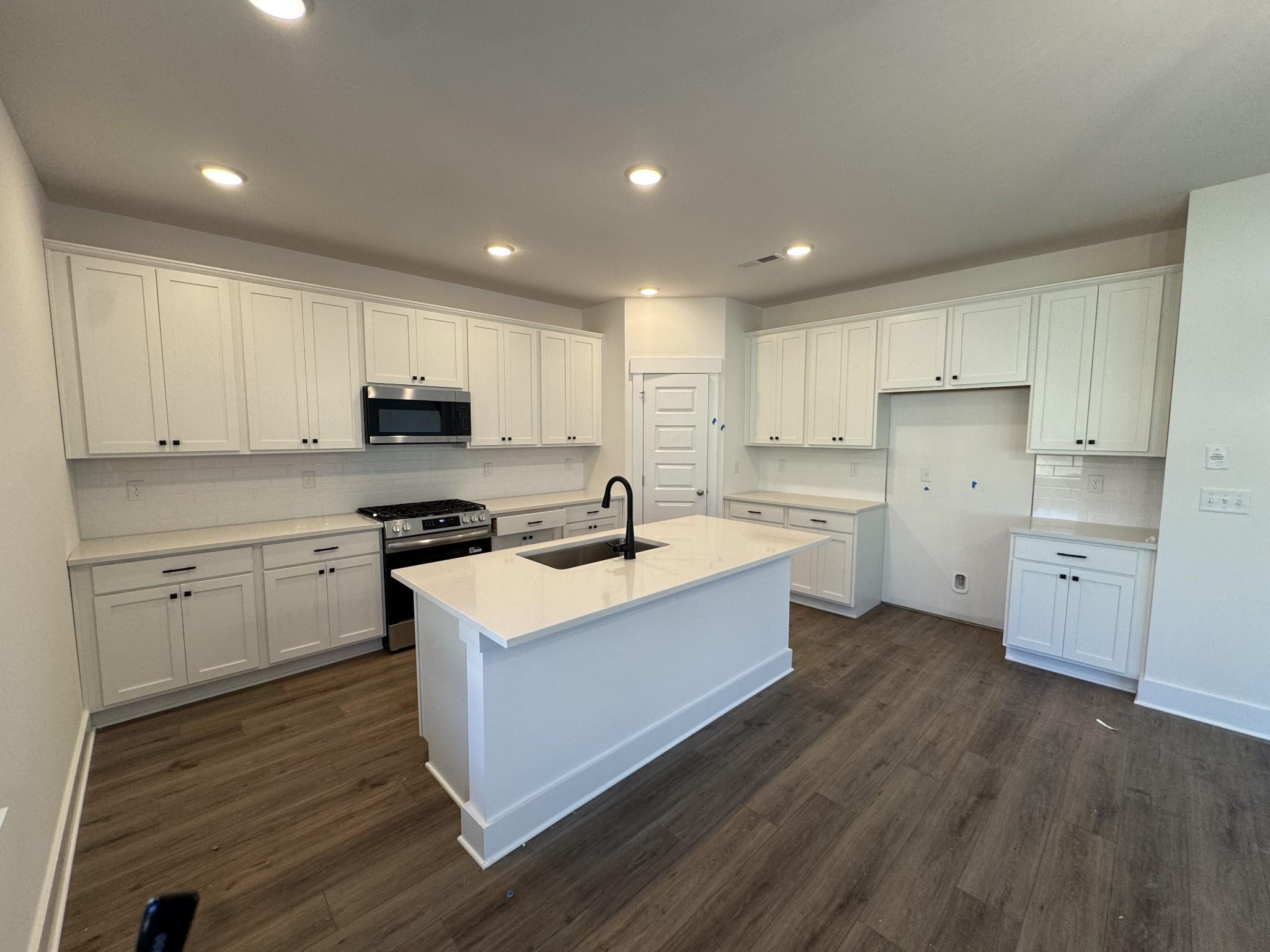Modern white kitchen with quartz island sink, stainless steel appliances, and shaker cabinets in The Logan C by Davidson Homes, Gallatin, TN