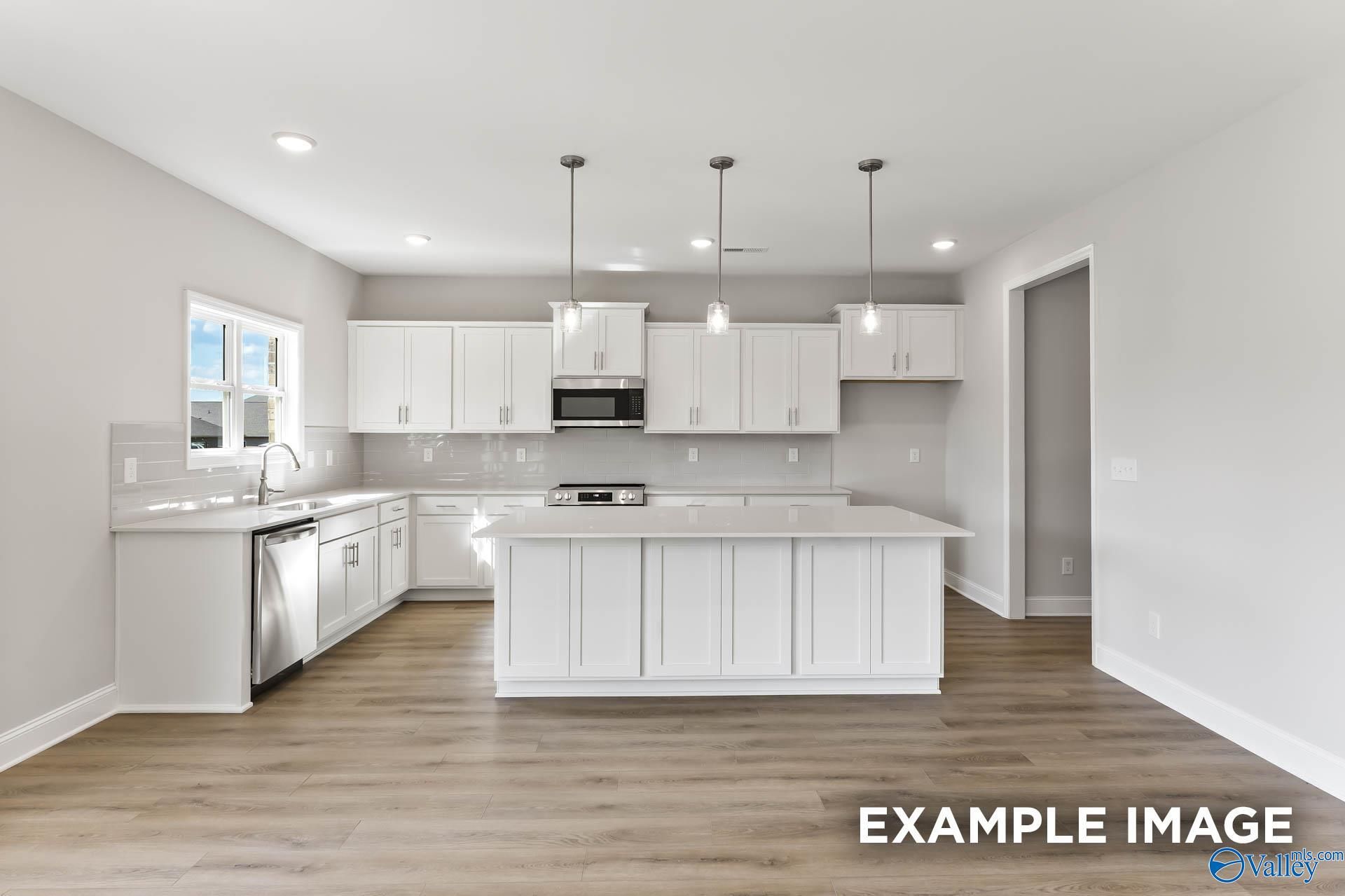 Modern white kitchen with large island, stainless steel appliances, and hardwood floors in The Chelsea D by Davidson Homes, New Market, AL