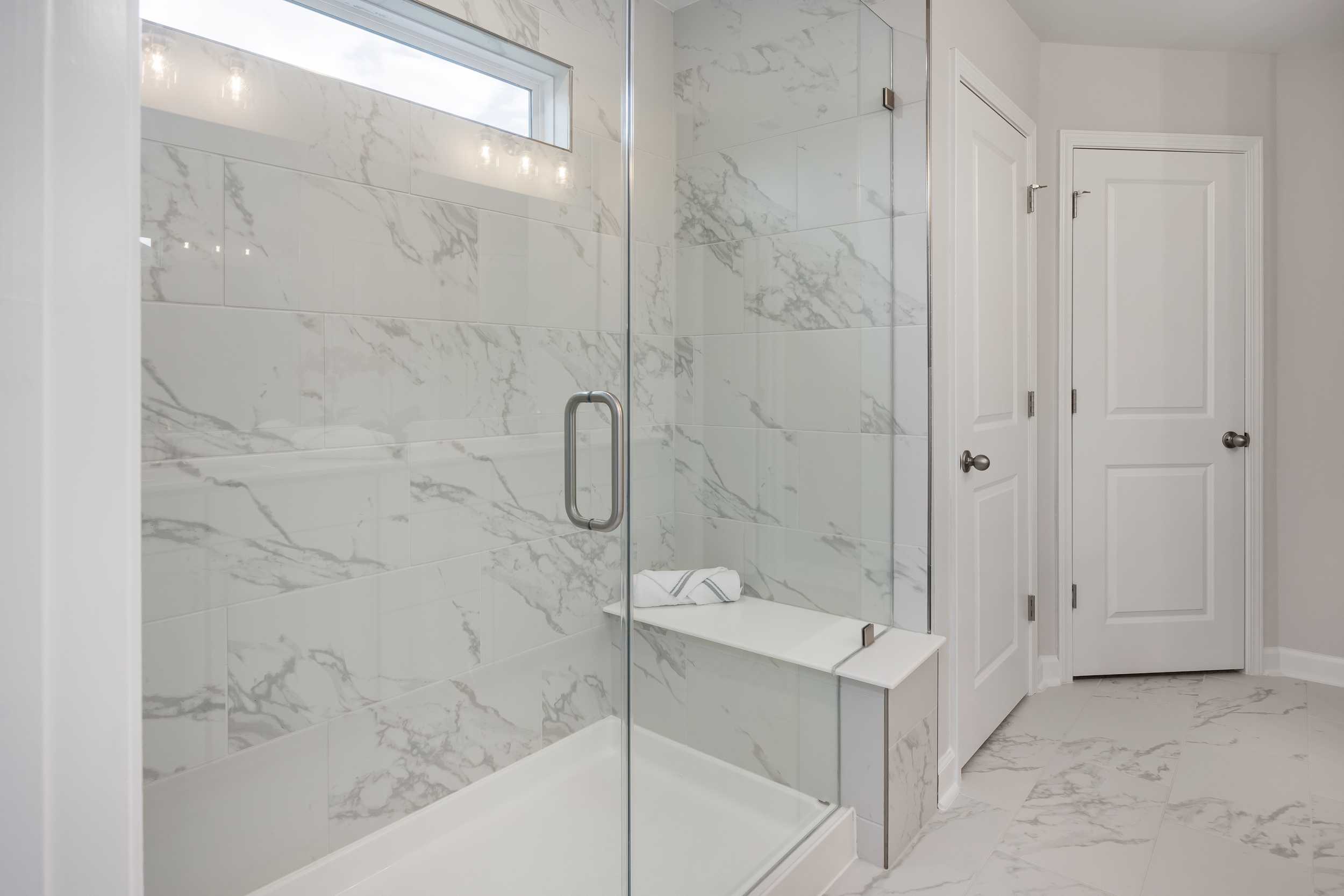 Luxurious marble-tiled walk-in shower with glass enclosure and built-in bench at Enclave at Belmont in Belmont, NC