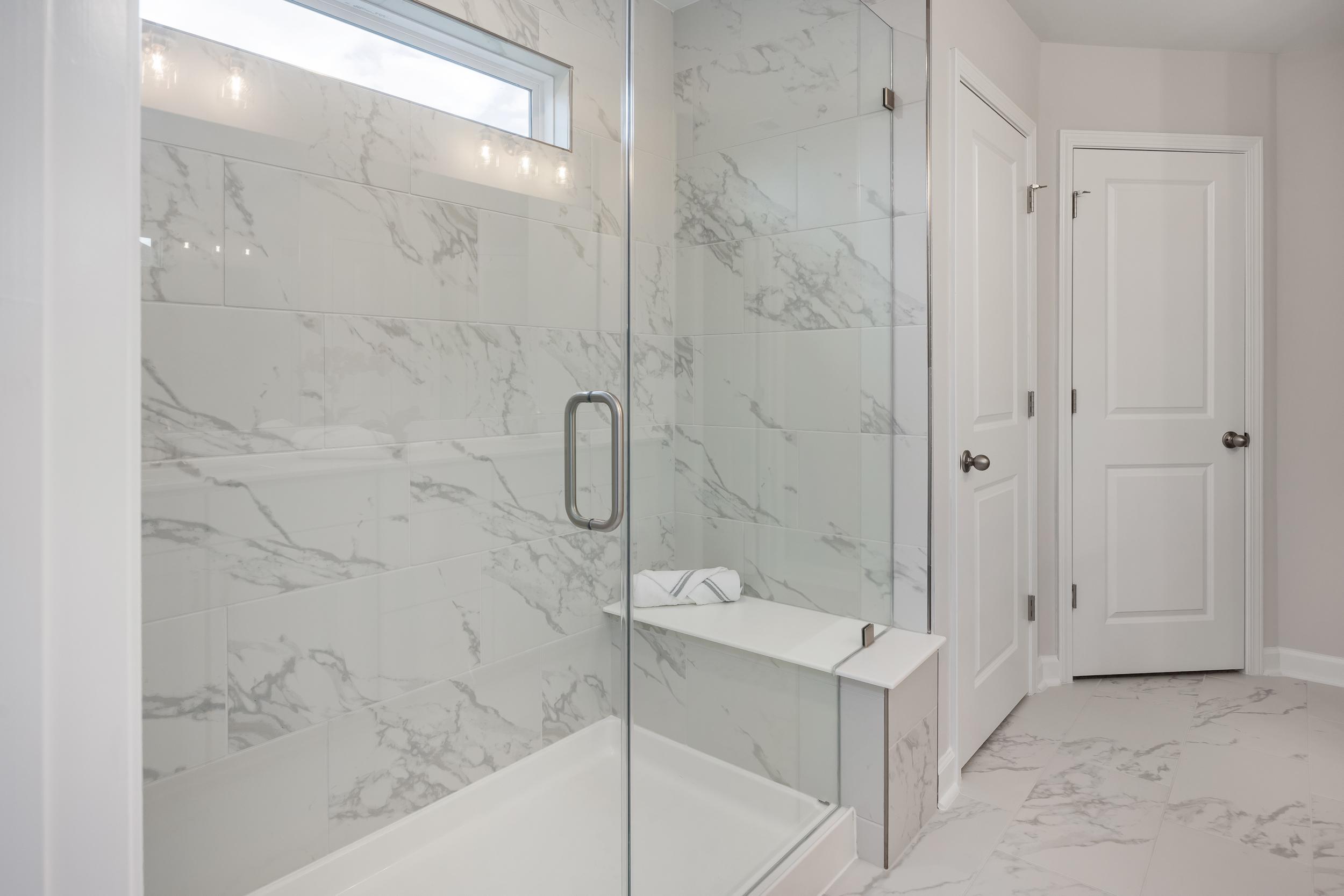 Luxurious marble-tiled walk-in shower with glass enclosure and built-in bench at Enclave at Belmont in Belmont, NC