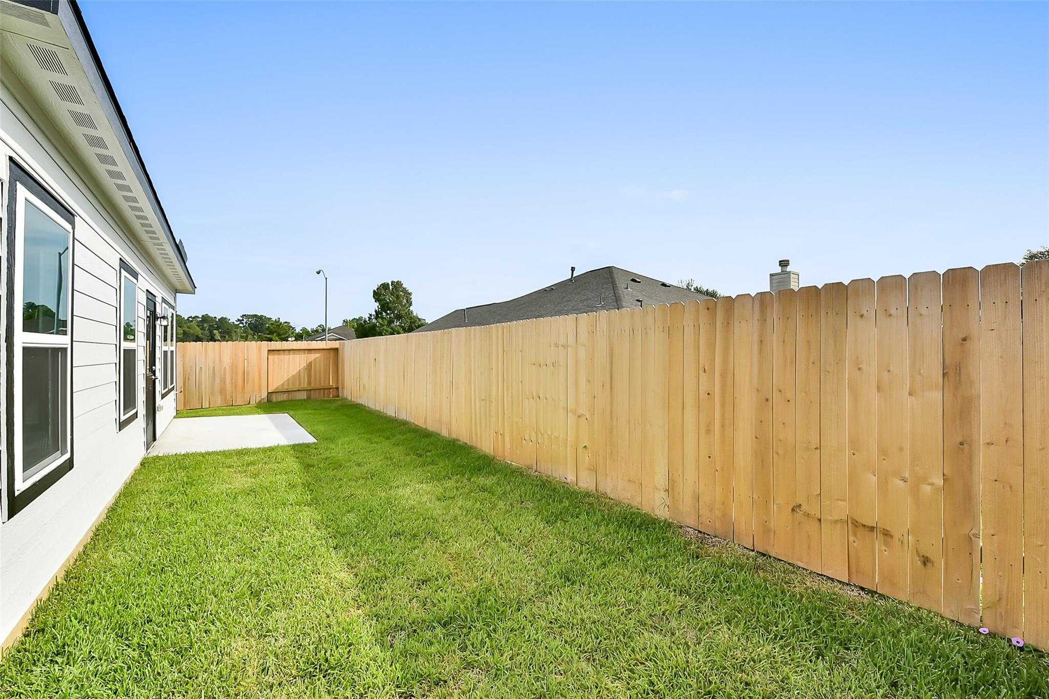 Backyard of 3-bedroom The Comal G home with green lawn, concrete patio, and wooden privacy fence in The Villages at WestPointe, Dayton, Texas