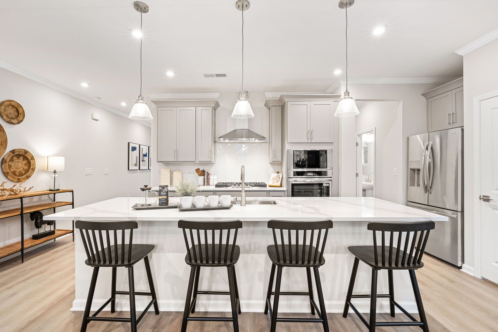 Spacious modern kitchen at Lake Shore in Winder GA featuring white shaker cabinets, quartz island, black stools, and stainless appliances
