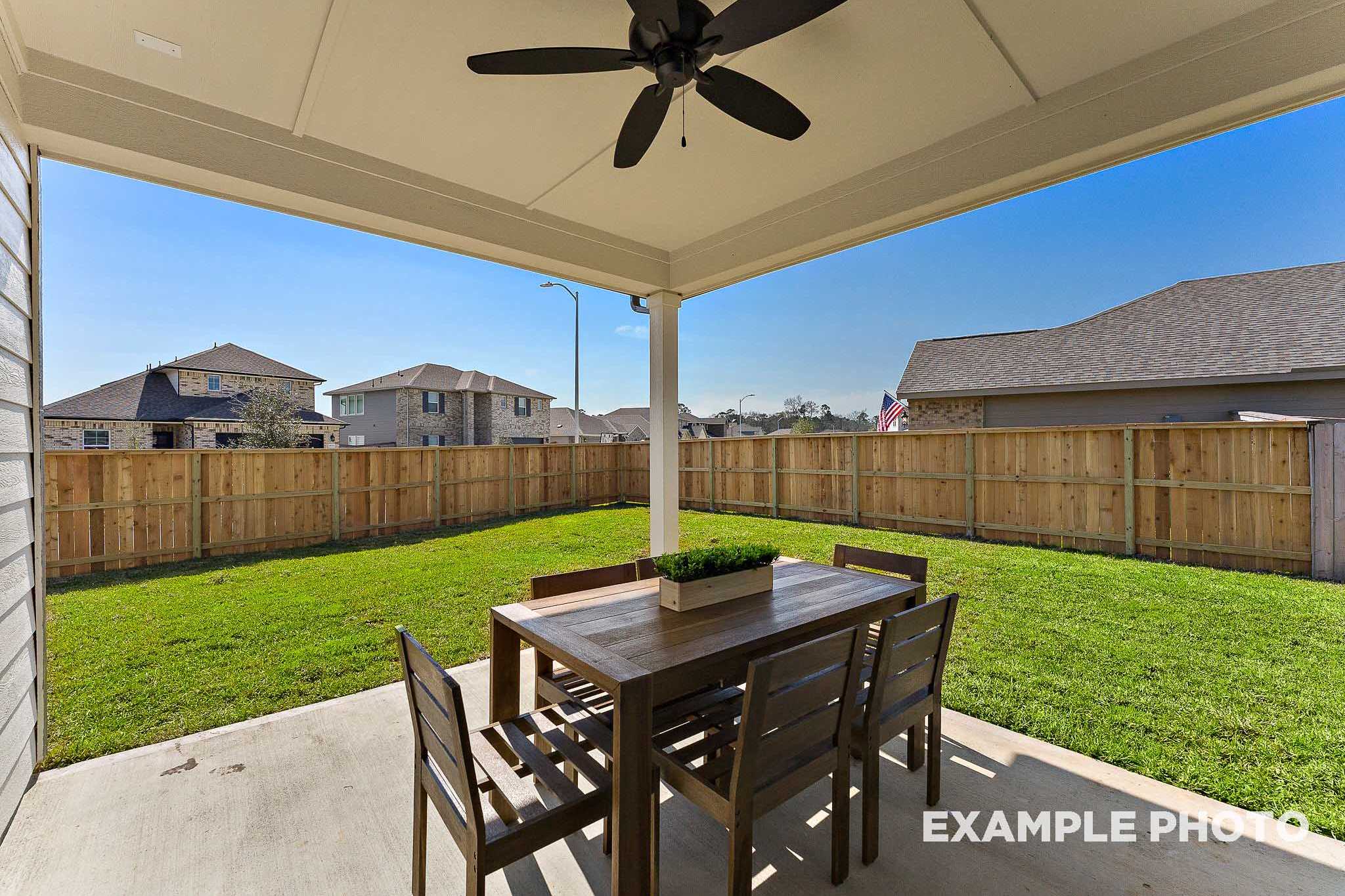 Spacious covered patio in The Everett E Davidson Homes design featuring wooden dining set, ceiling fan, lush green lawn, and privacy fence