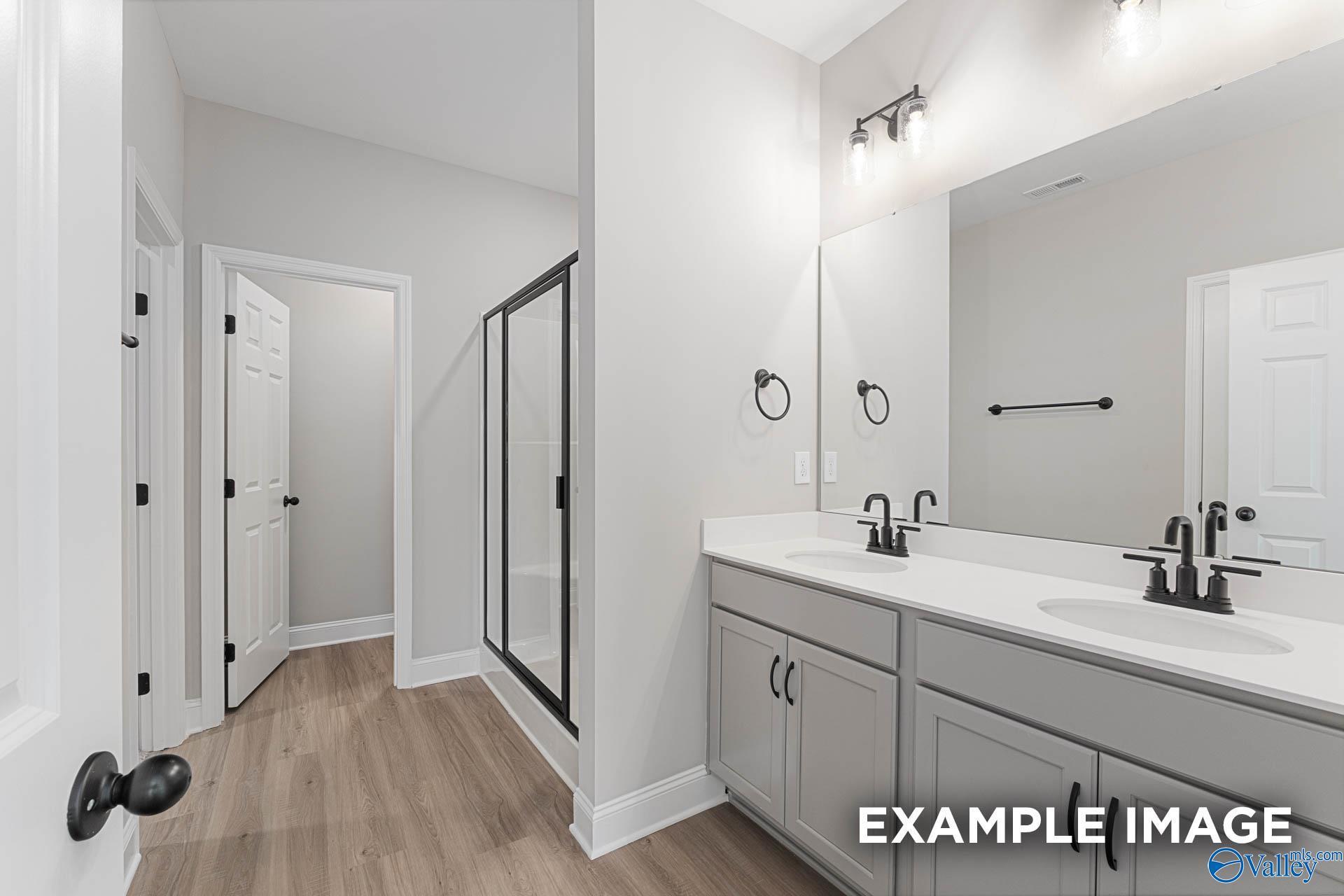 Modern master bathroom featuring double vanity sinks, frameless glass shower, and wood flooring in Davidson Homes The Daphne D, Meridianville, Alabama