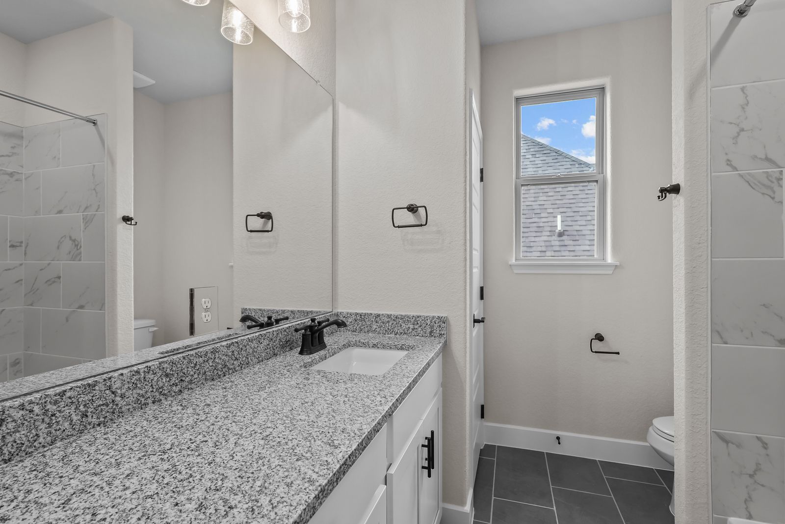 Modern bathroom in The Belmont featuring granite vanity, white cabinetry, and tiled shower in Castroville, Texas.