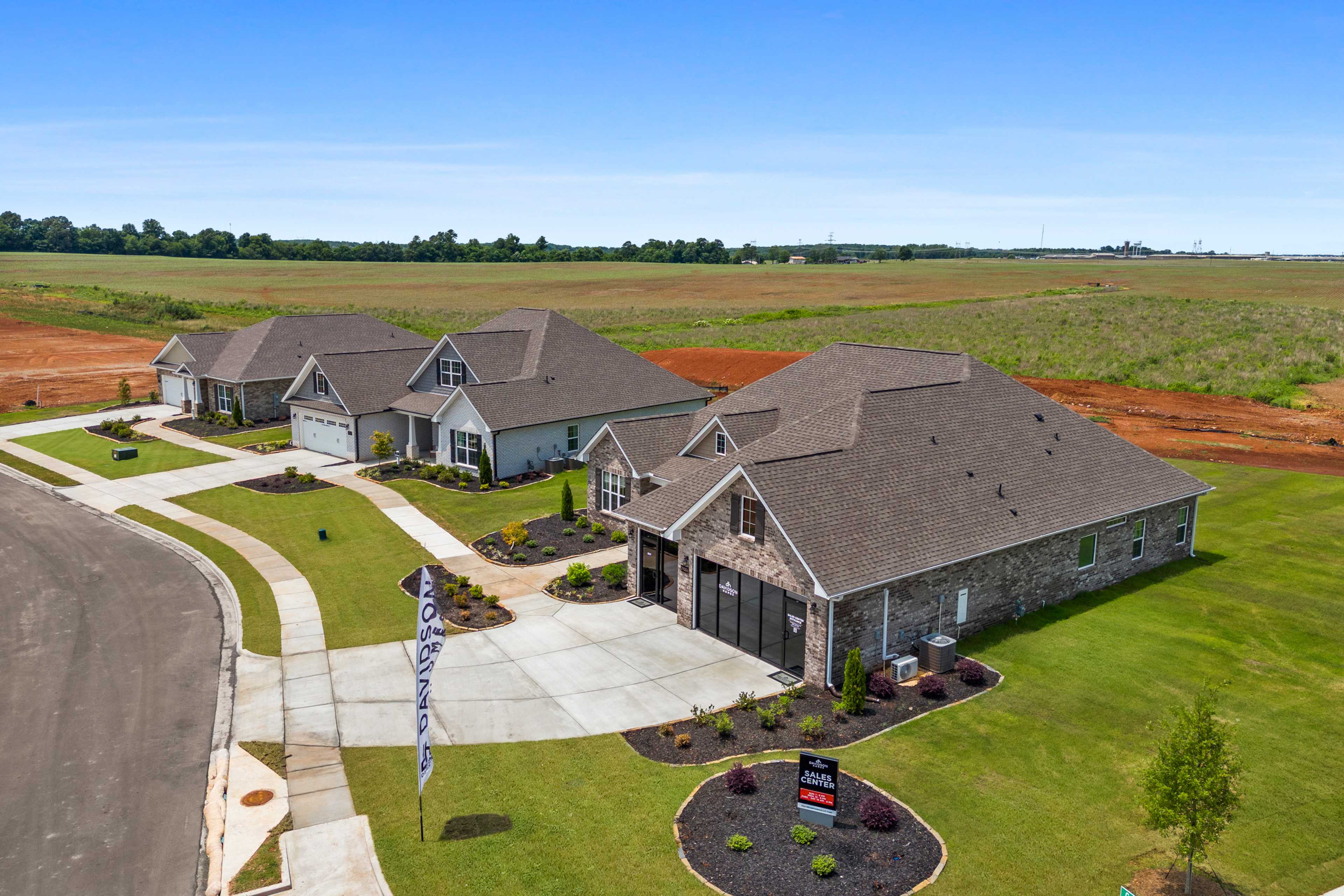 Aerial view of new homes at Creekside in Harvest Alabama featuring stone accents garages driveways and landscaping amid fields