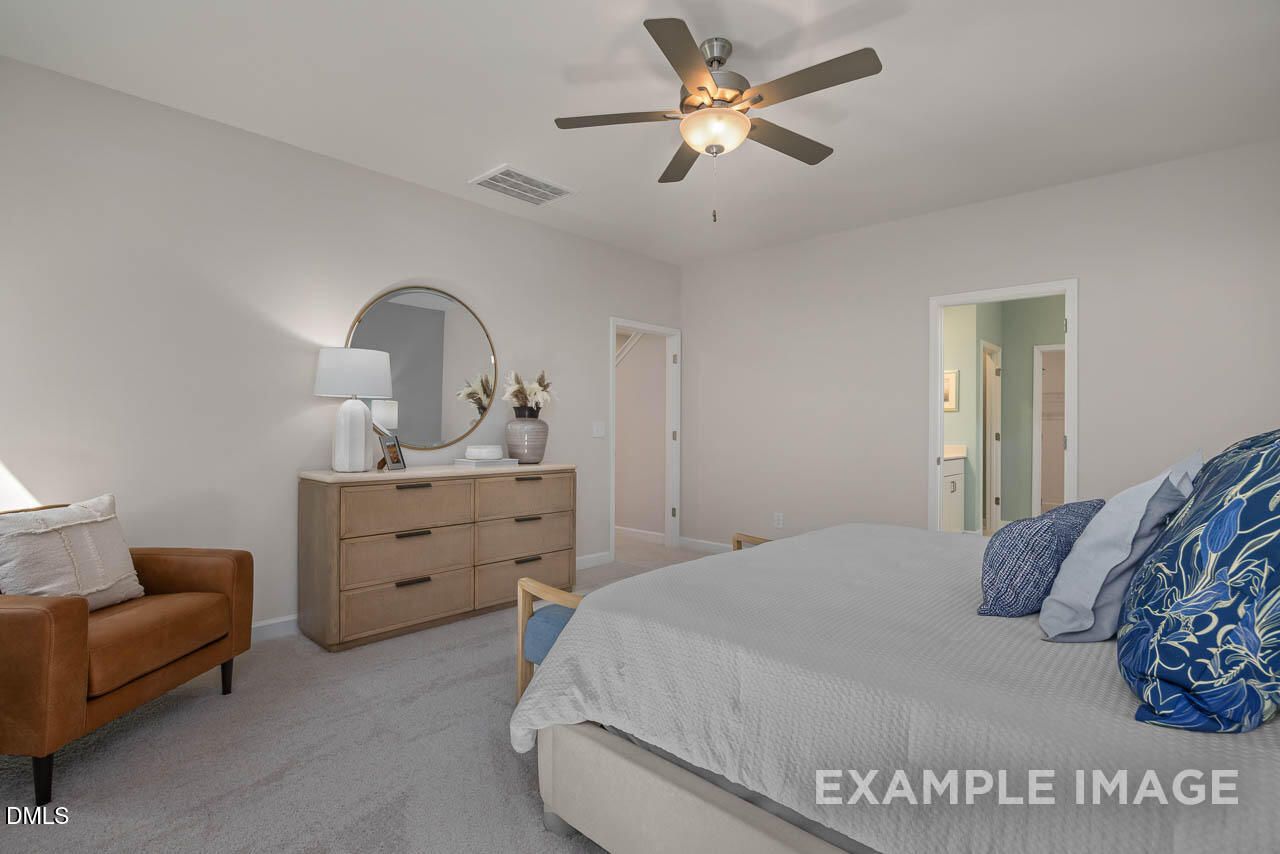 Cozy master bedroom with king bed, blue pillows, wooden dresser, round mirror, ceiling fan, and en-suite bath in Davidson Homes The Hickory II C, Wake Forest, NC