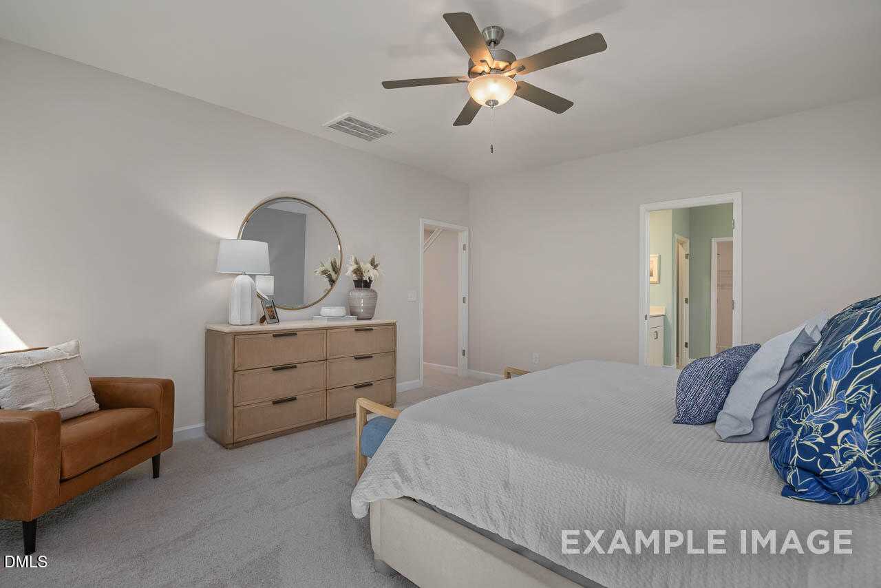 Cozy master bedroom with king bed, blue pillows, wooden dresser, round mirror, ceiling fan, and en-suite bath in Davidson Homes The Hickory II C, Wake Forest, NC