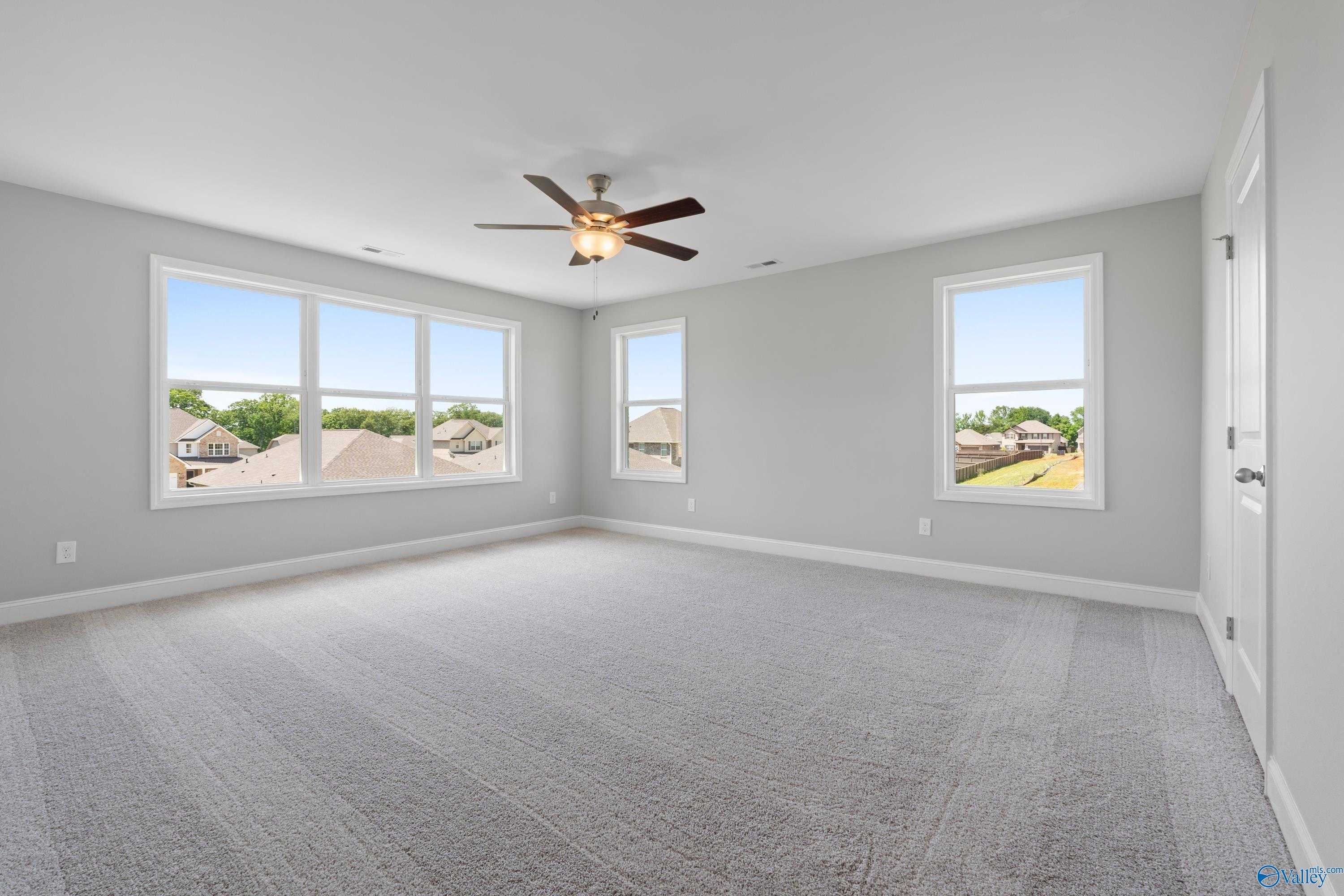 Spacious empty bedroom with large windows overlooking neighborhood, ceiling fan, gray walls, and carpet in Davidson Homes The Chelsea B, New Market, Alabama
