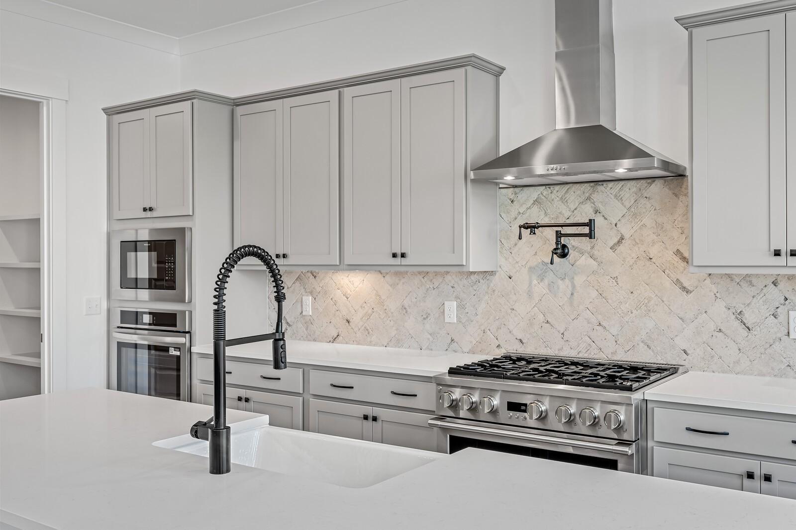 Modern gray shaker kitchen with white quartz island, stainless gas range, pull-out faucet, and subway tile backsplash in The Alston A, Murfreesboro, TN