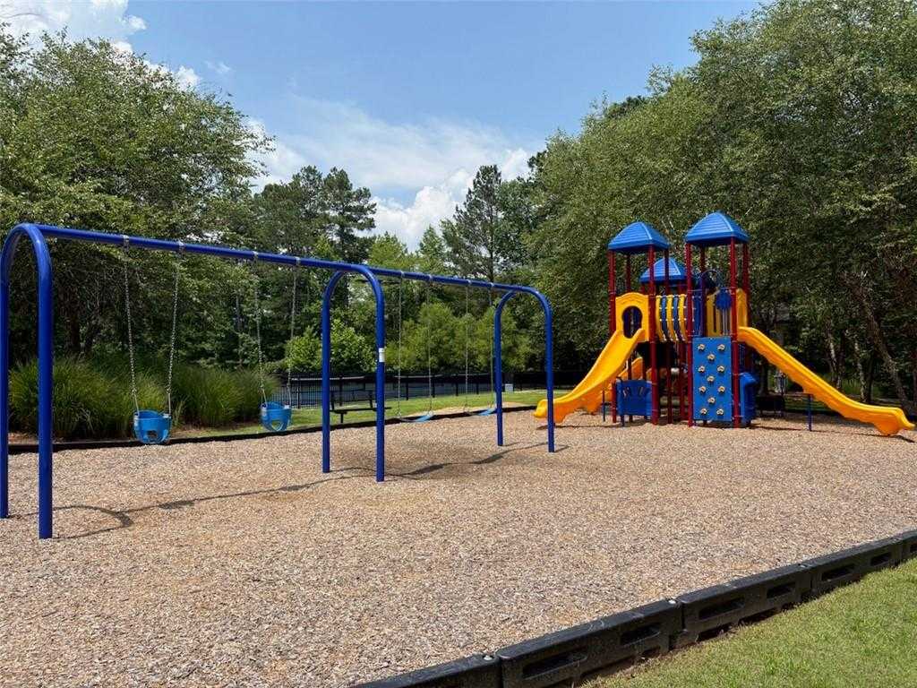 Vibrant playground with blue swings, yellow slides, and climbing tower amid trees in Riverwood, Dallas, Georgia community