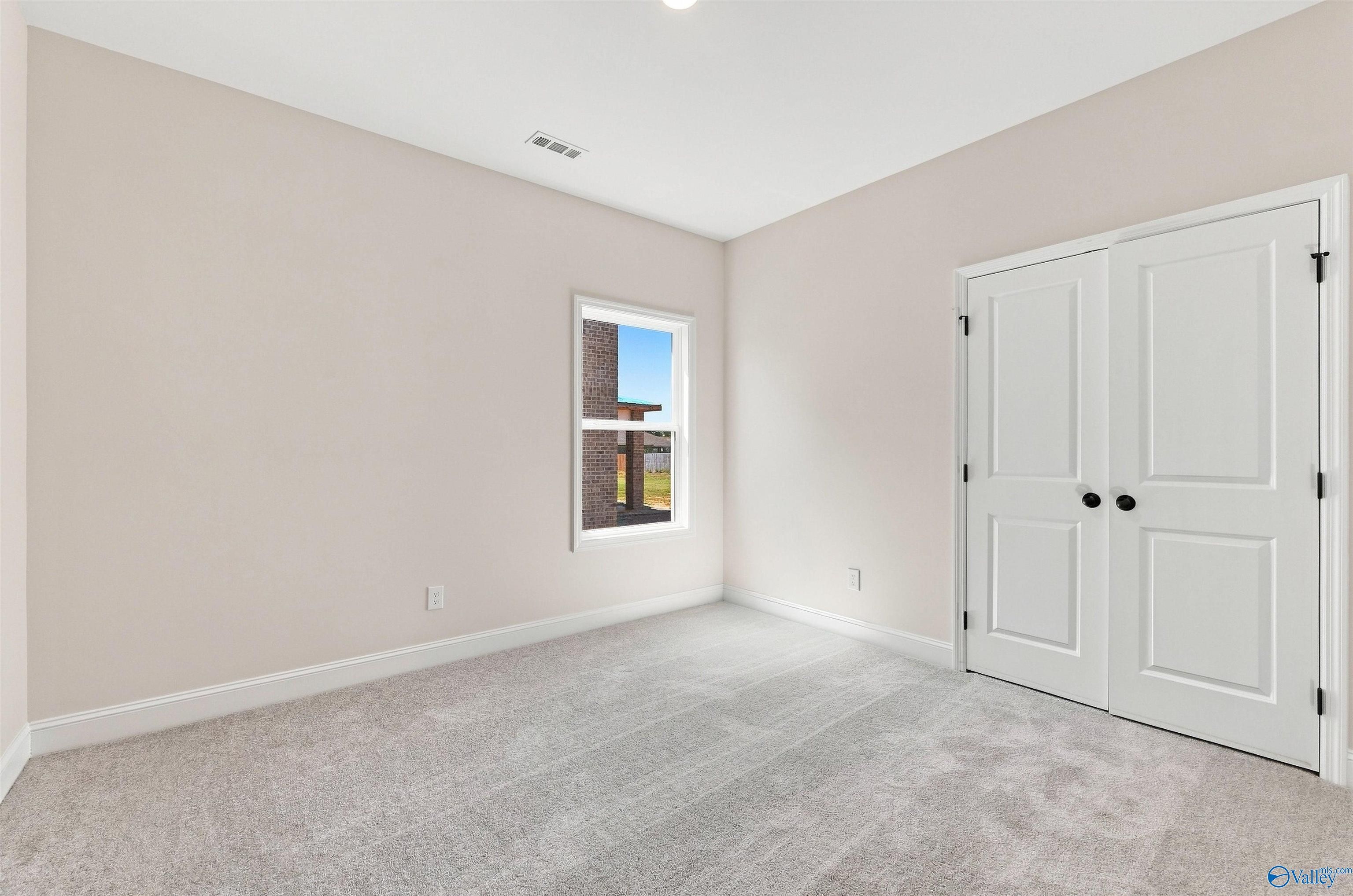 Bright neutral bedroom with gray carpet, white double-door closet, and window in Davidson Homes The Everett B, Toney, Alabama