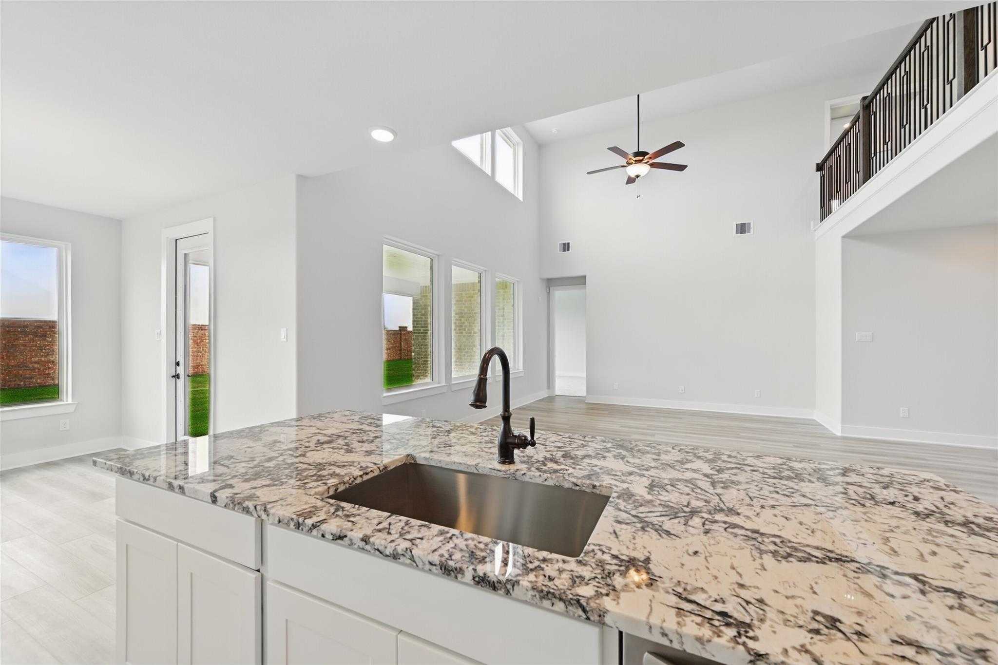 Modern open kitchen with granite island, stainless sink, high ceilings, and backyard view in Davidson Homes Victoria C, Lago Mar, Texas City