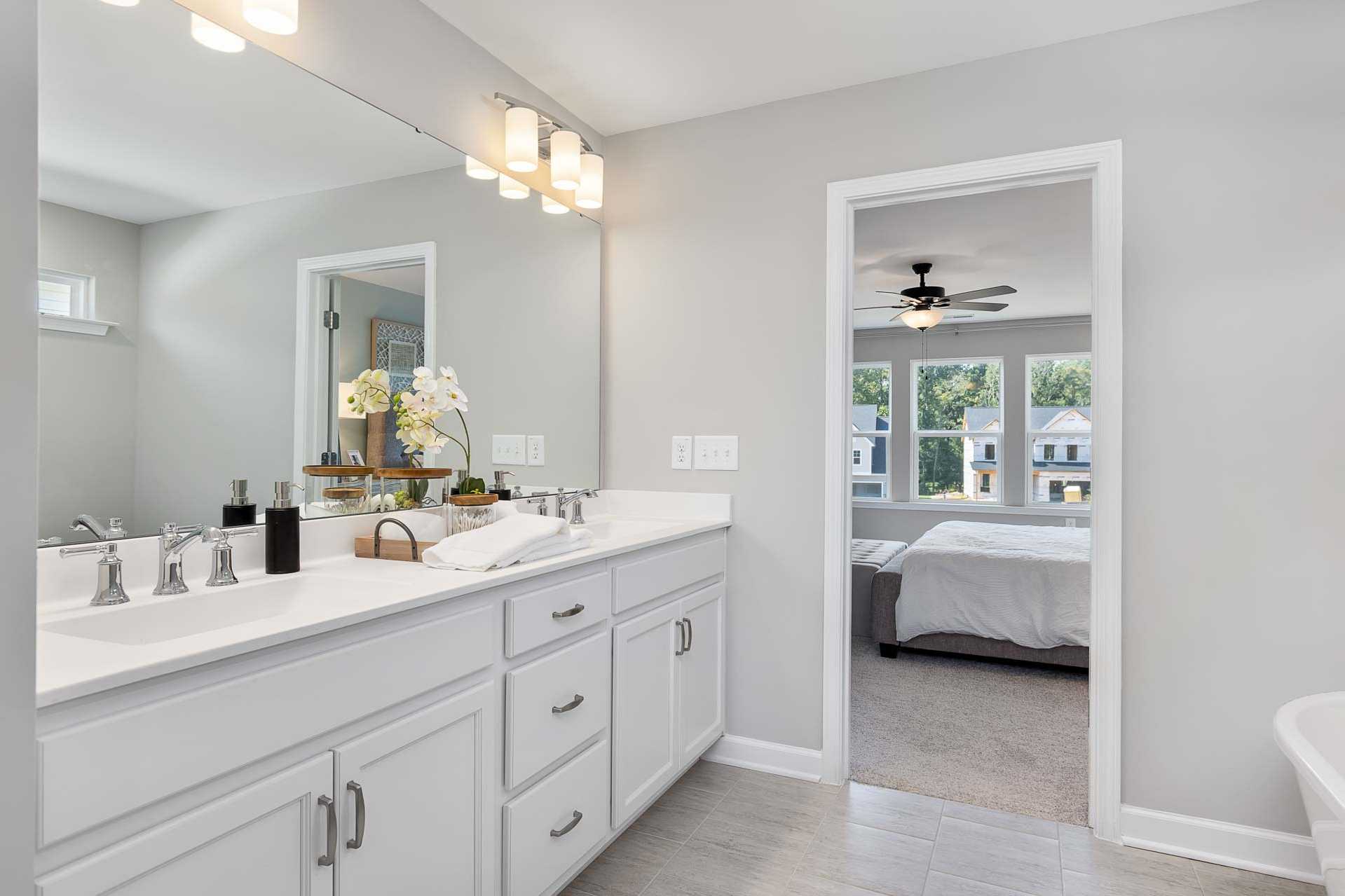 Spacious master bathroom at Highland Forest in Fuquay-Varina NC with double white vanity, orchids, and open bedroom view