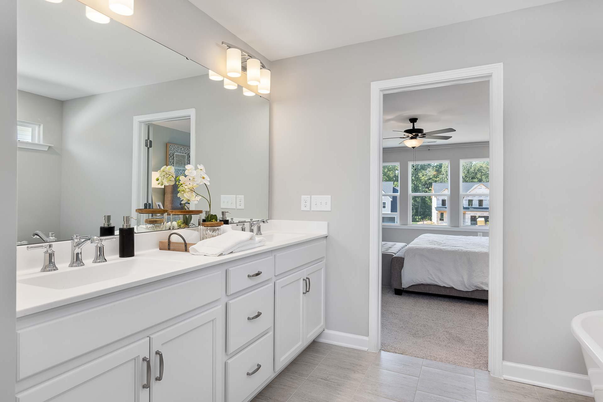 Spacious master bathroom at Highland Forest in Fuquay-Varina NC with double white vanity, orchids, and open bedroom view