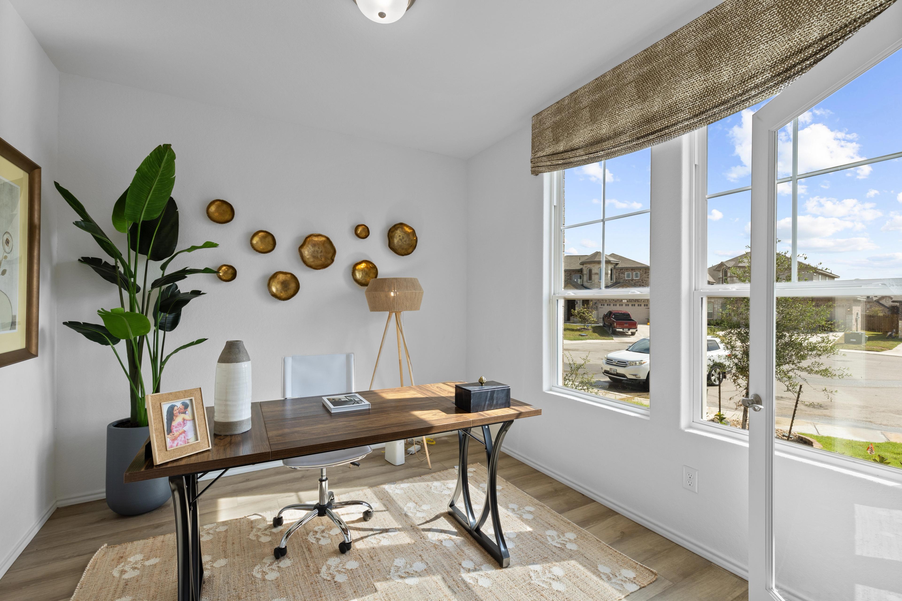 Spacious home office at Horizon Pointe in Converse, Texas by Davidson Homes featuring wooden desk, potted plants, gold wall decor, and neighborhood view