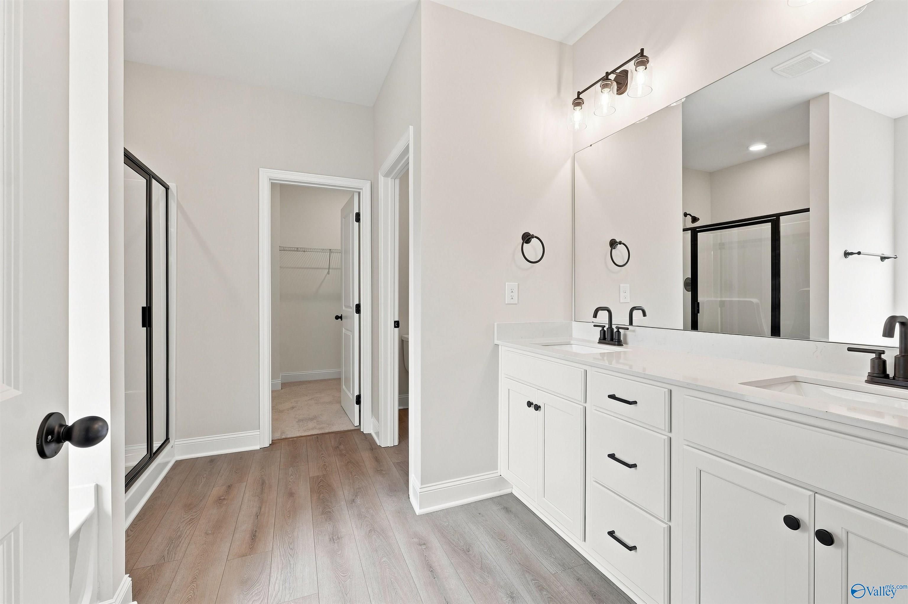 Primary bathroom with double vanity, white cabinetry, matte black fixtures, and walk-in shower in The Everett B, Toney, Alabama