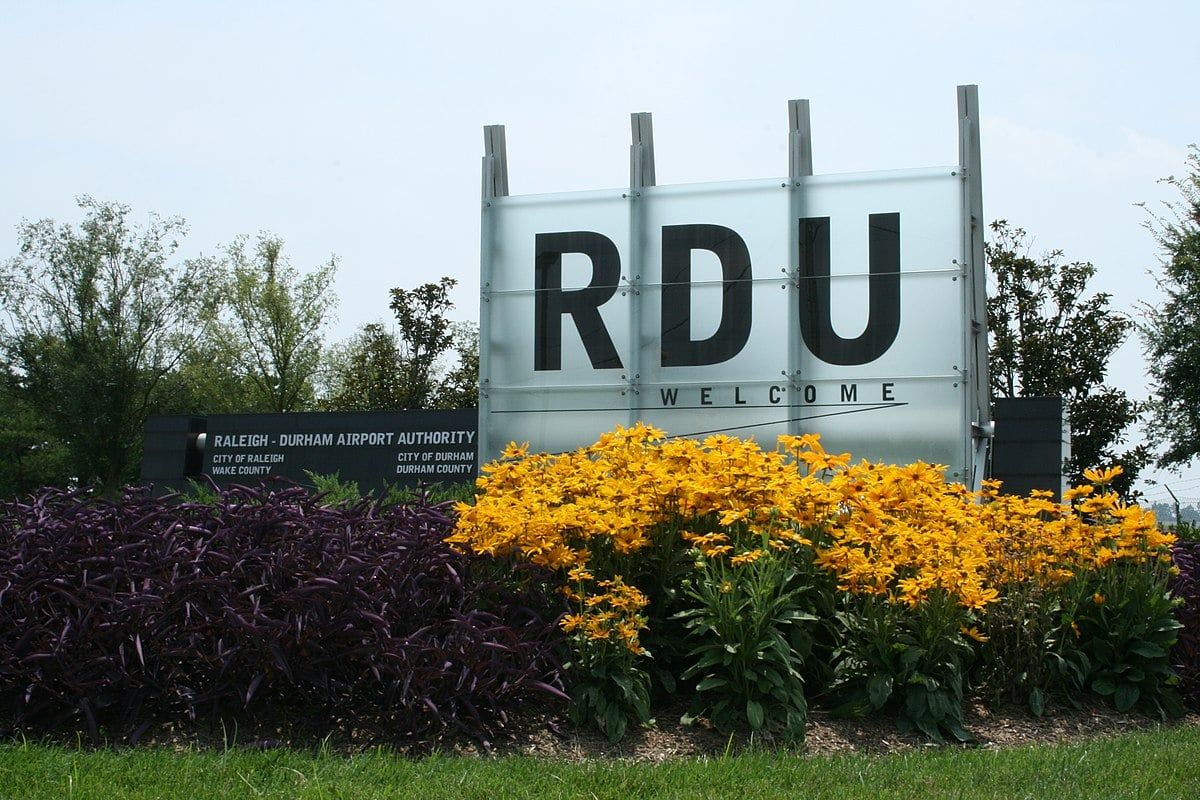 RDU welcome sign at Raleigh-Durham Airport with frosted glass letters, yellow black-eyed Susans, purple shrubs, and trees near Forestville Yard Knightdale NC