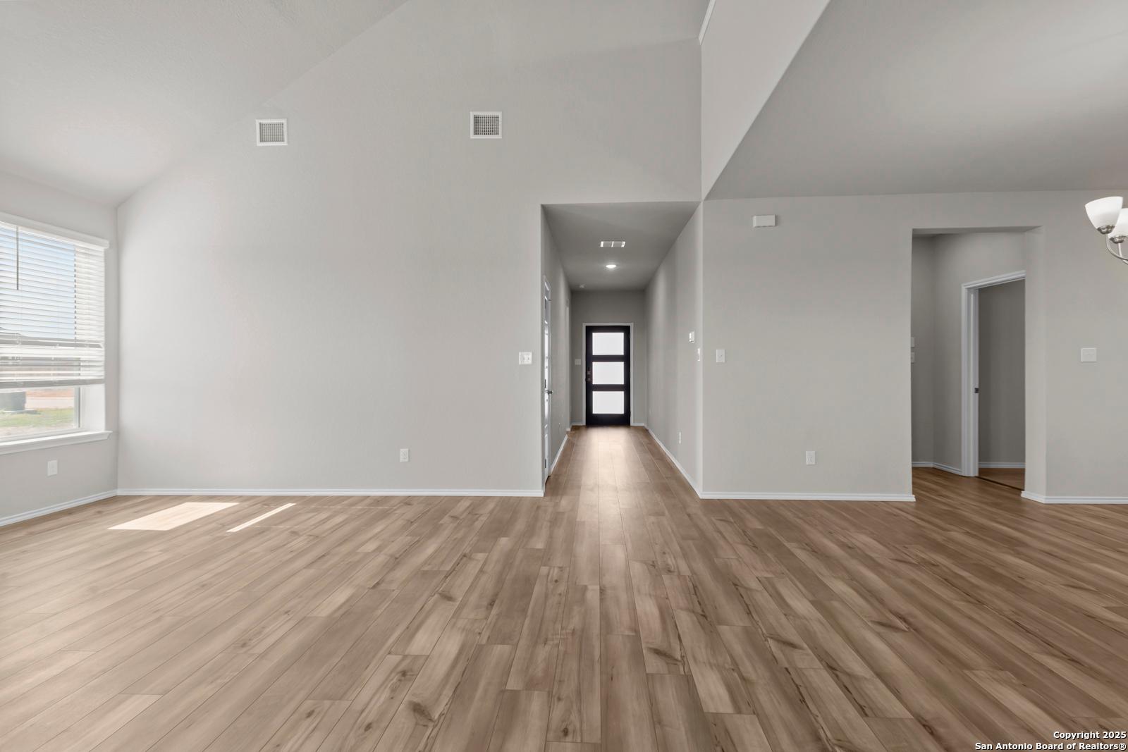 Spacious entry hallway with light hardwood floors, vaulted ceilings, and modern black door in The Collin B home, Seguin, Texas