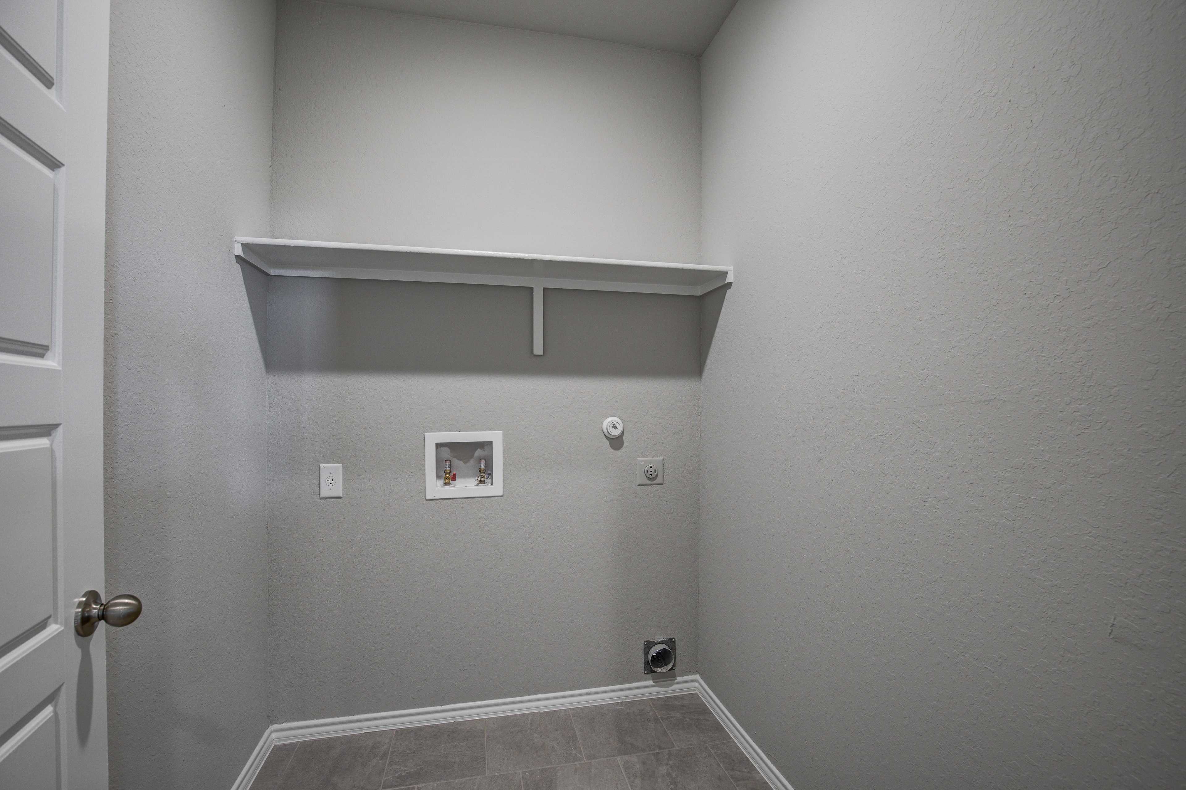 Spacious laundry room in The Blanco B with gray walls, white built-in shelves, washer-dryer hookups, and beige tile floor