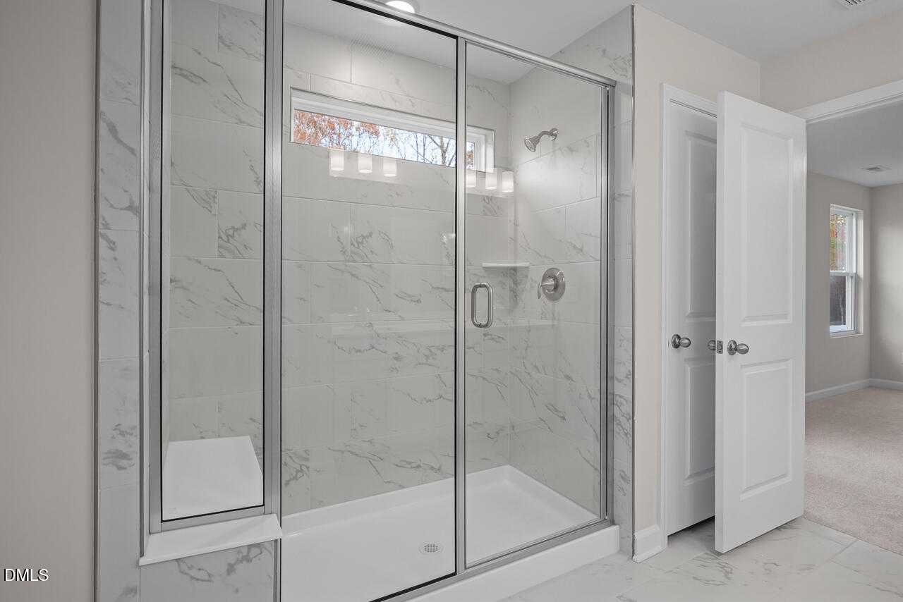Modern frameless glass shower with marble tiles and bench in master bath of Davidson Homes The Gavin C, Lillington, NC