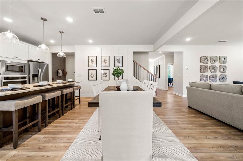 Open-concept kitchen with white cabinets, stainless appliances, island bar, dining table, and adjacent living room in Davidson Homes The Willow B, Dallas, Georgia