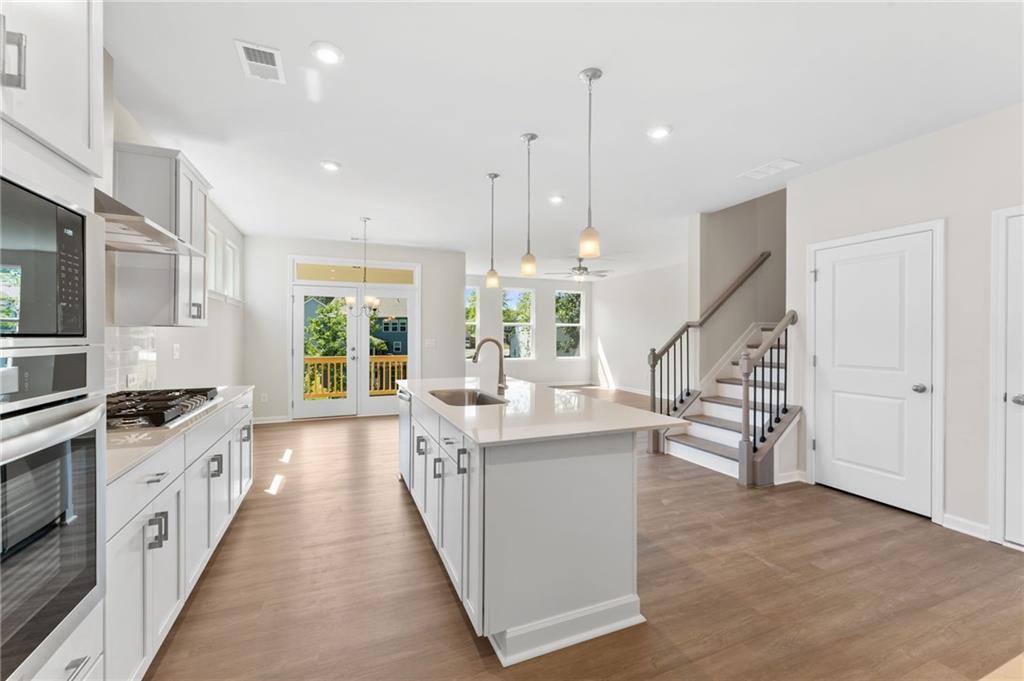 Modern open-concept kitchen with white island, stainless appliances, French doors to deck, and hardwood floors in Davidson Homes The Ash B, Dallas, GA
