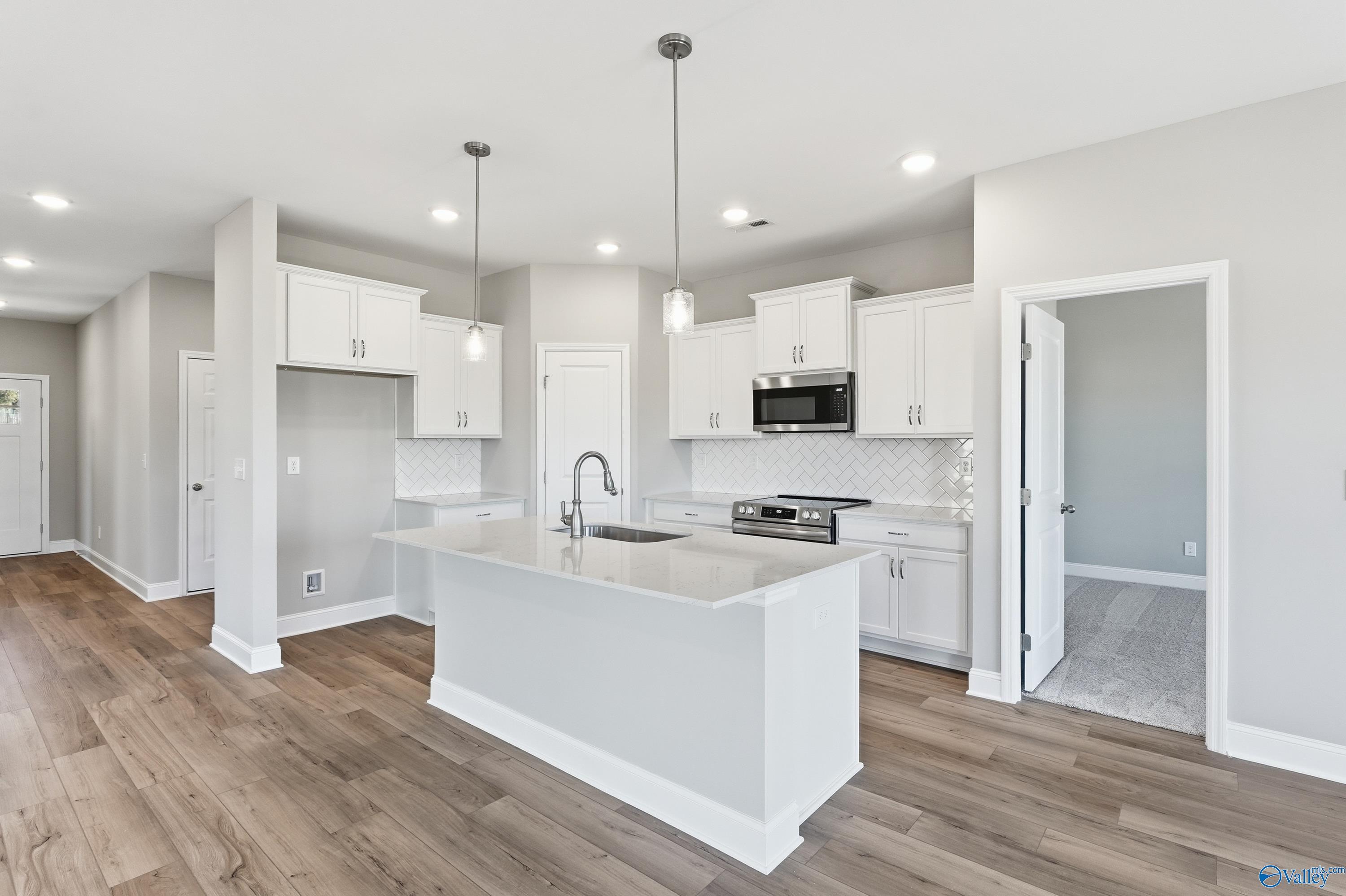 Bright open-concept kitchen with white shaker cabinets, quartz island sink, stainless appliances in Davidson Homes The Franklin C, New Market, AL