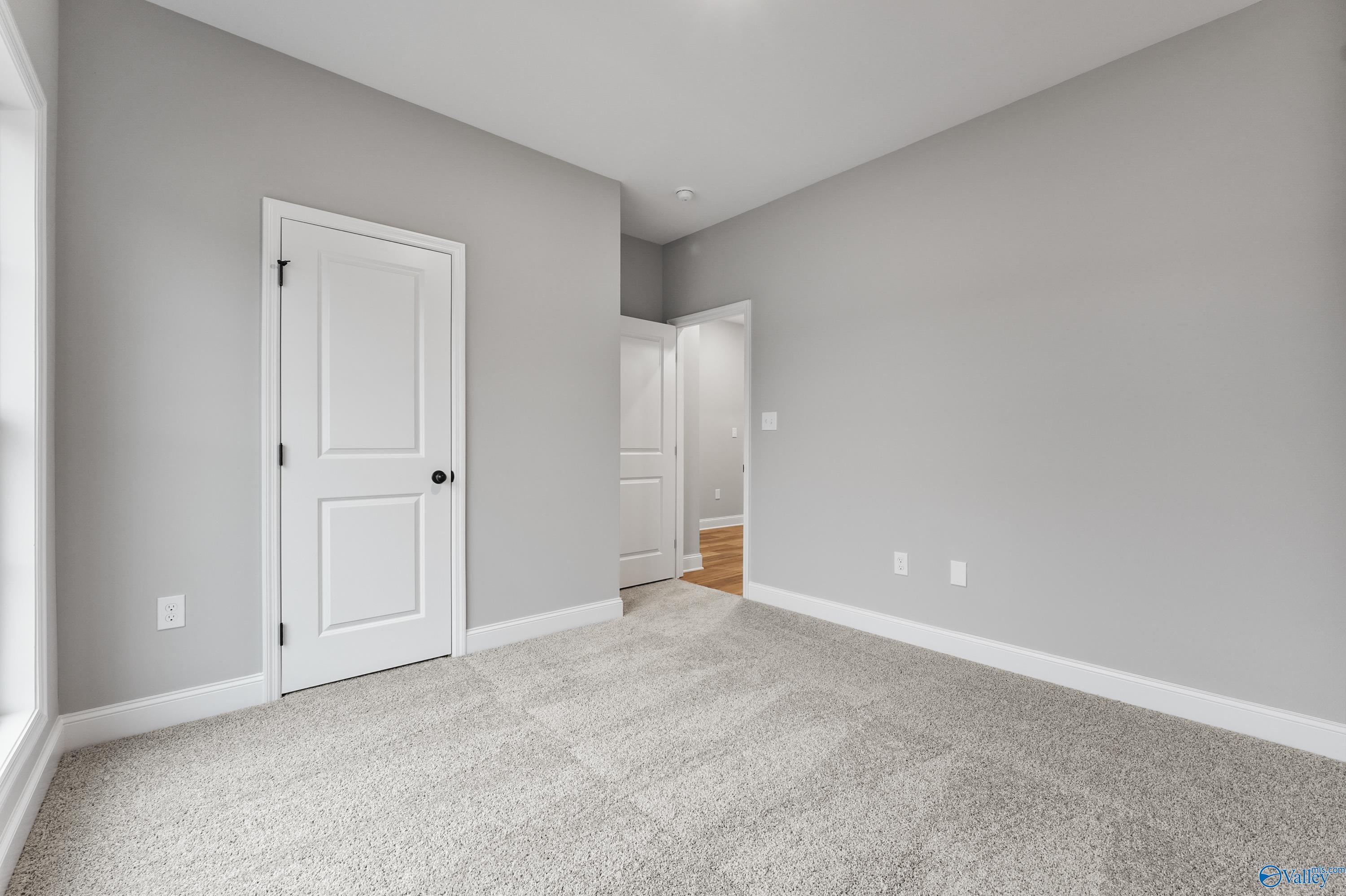 Empty bedroom with light gray walls, white doors, carpeted floor in Davidson Homes The Asheville C, Meridianville, Alabama