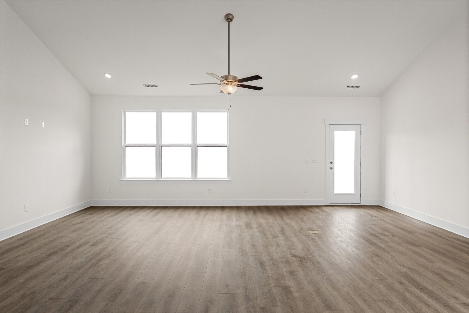 Bright empty living room with hardwood floors, large windows, glass door, and ceiling fan in Davidson Homes Ridgeport D, Mt. Juliet, Tennessee